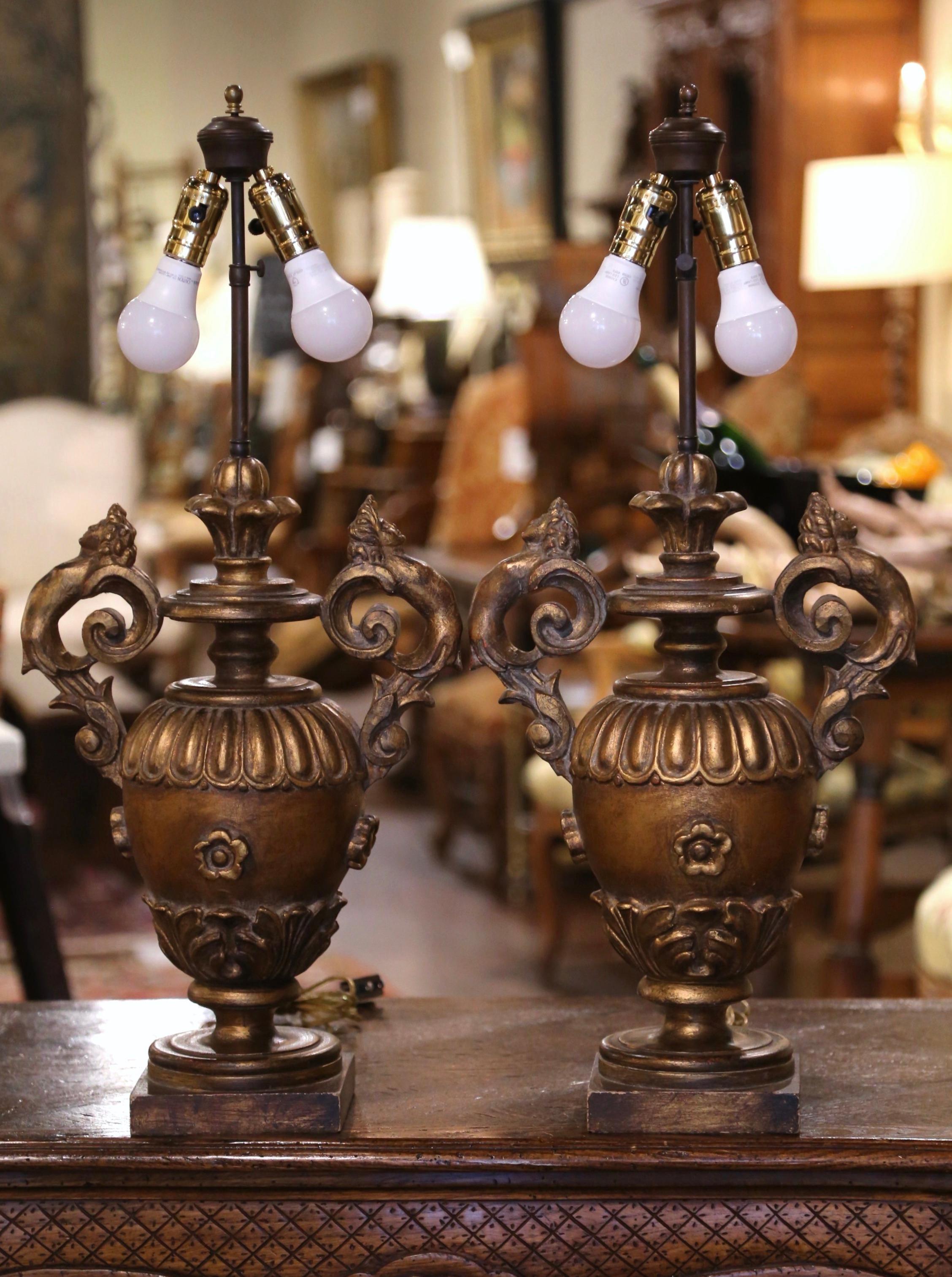 Place these elegant antique lamps on bedside tables or on top of a console in an entry! Crafted in Italy circa 1970, each lamp sits on a square bottom over an gadrooned urn form base, dressed with acanthus leaf handles and decorated with hand carved