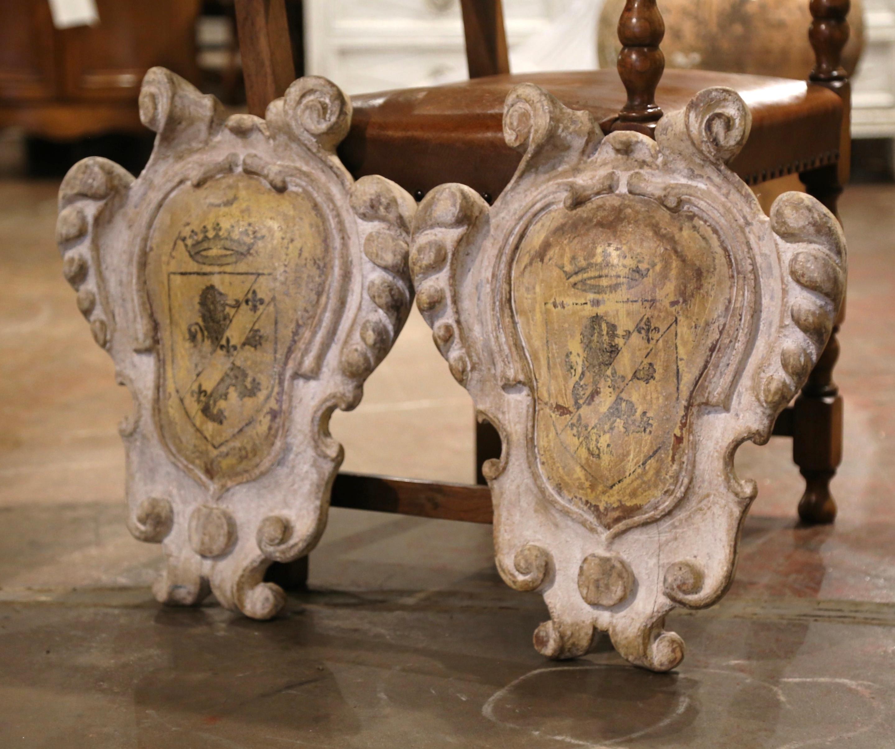 Decorate a game room or a study with this elegant pair of carved antique plaques. Crafted in southern Italy circa 1960, the  wall plaques feature a center oval medallion decorated with a hand painted family crest- a lion in a shield, a Fleur-de-Lys