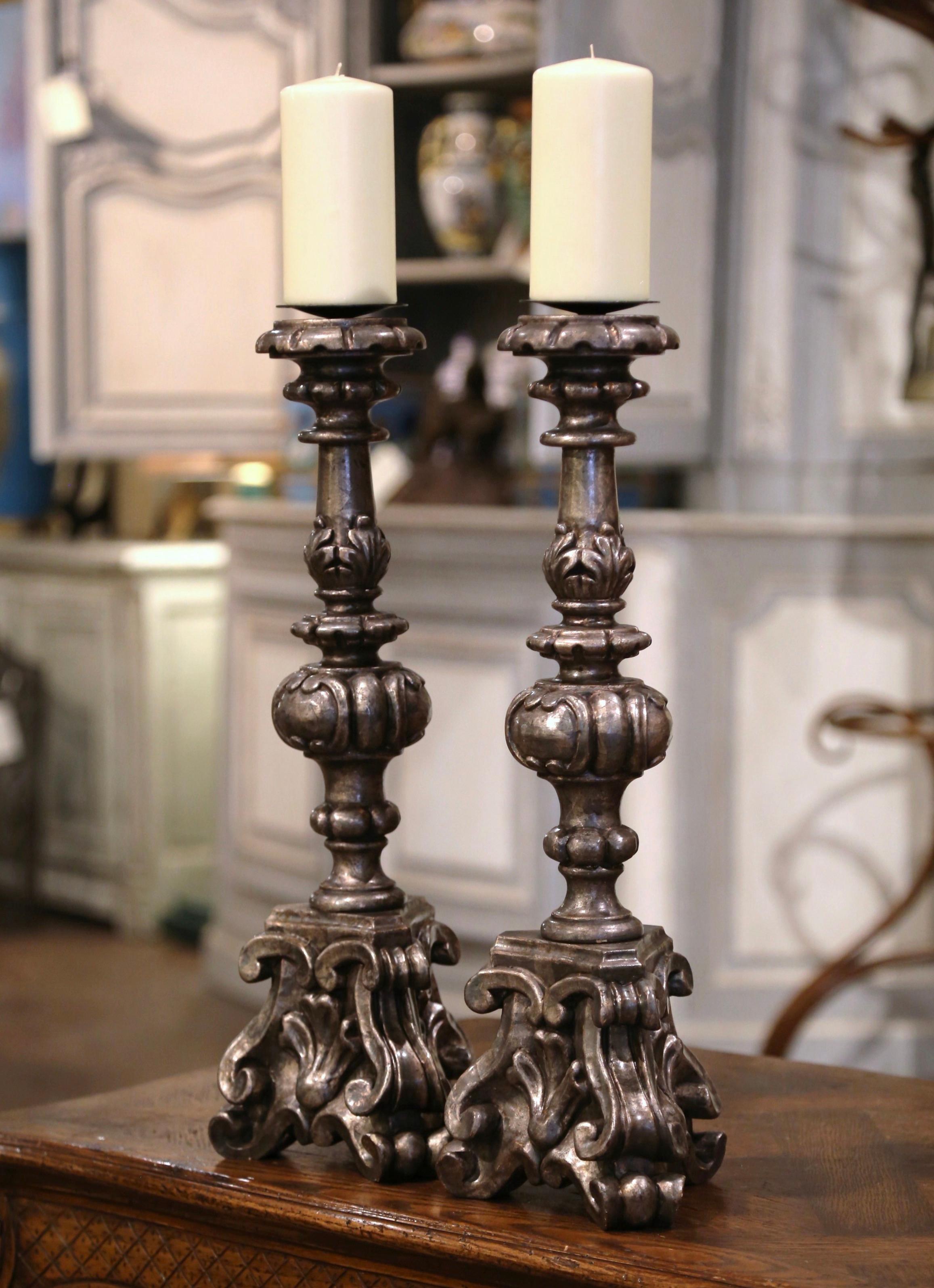 Add an air of drama and elegance to your home with this pair of antique candlesticks. Crafted in Italy circa 1960, each candle holder stands on a sturdy triangle base with hand carved acanthus leaves over three scrolled feet, and a tall carved