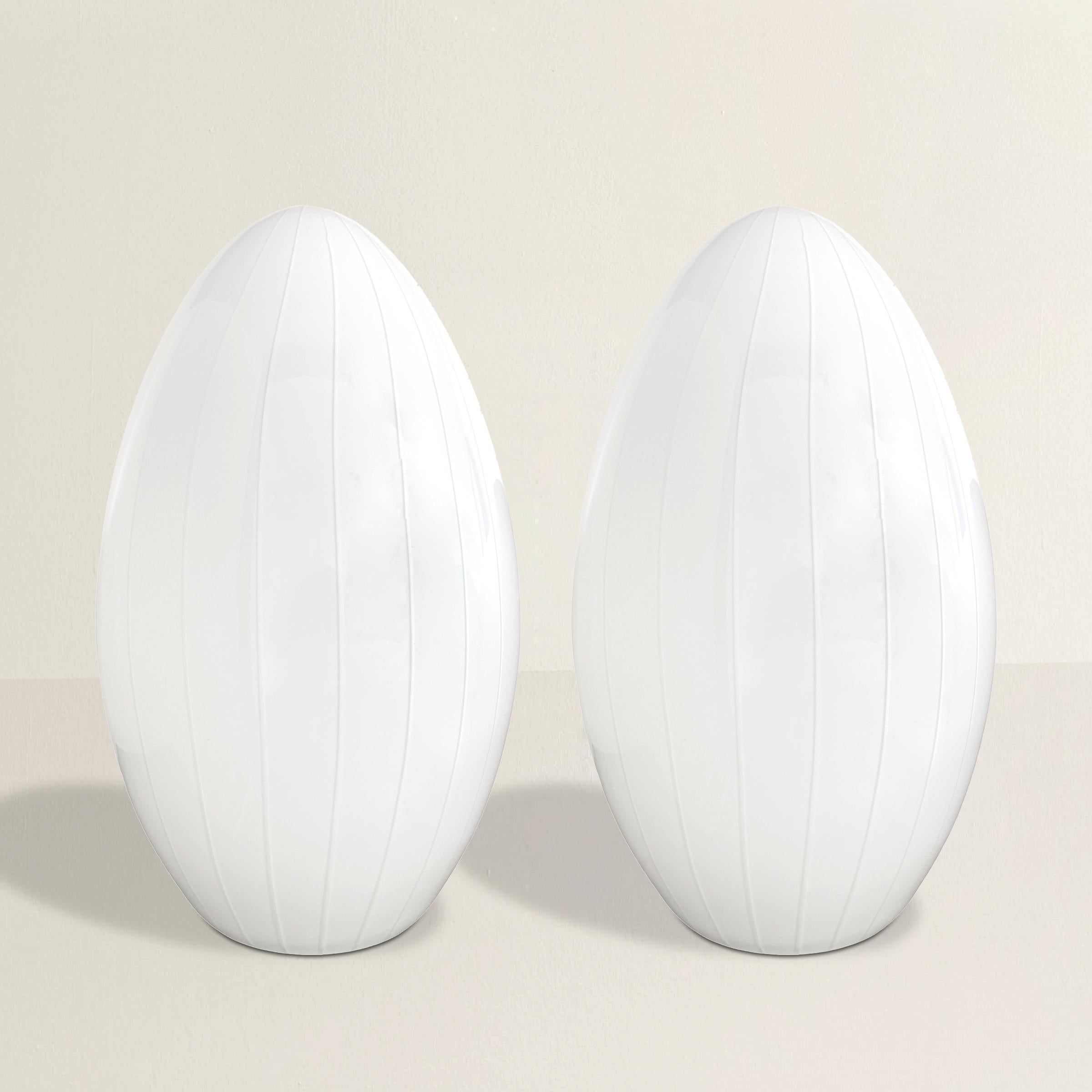 Questa elegante coppia di lampade a uovo Effetre Murano della metà del XX secolo mette in mostra la squisita maestria degli artigiani del vetro di Murano. Ogni lampada è dotata di un paralume in vetro bianco opaco con delicate striature verticali,
