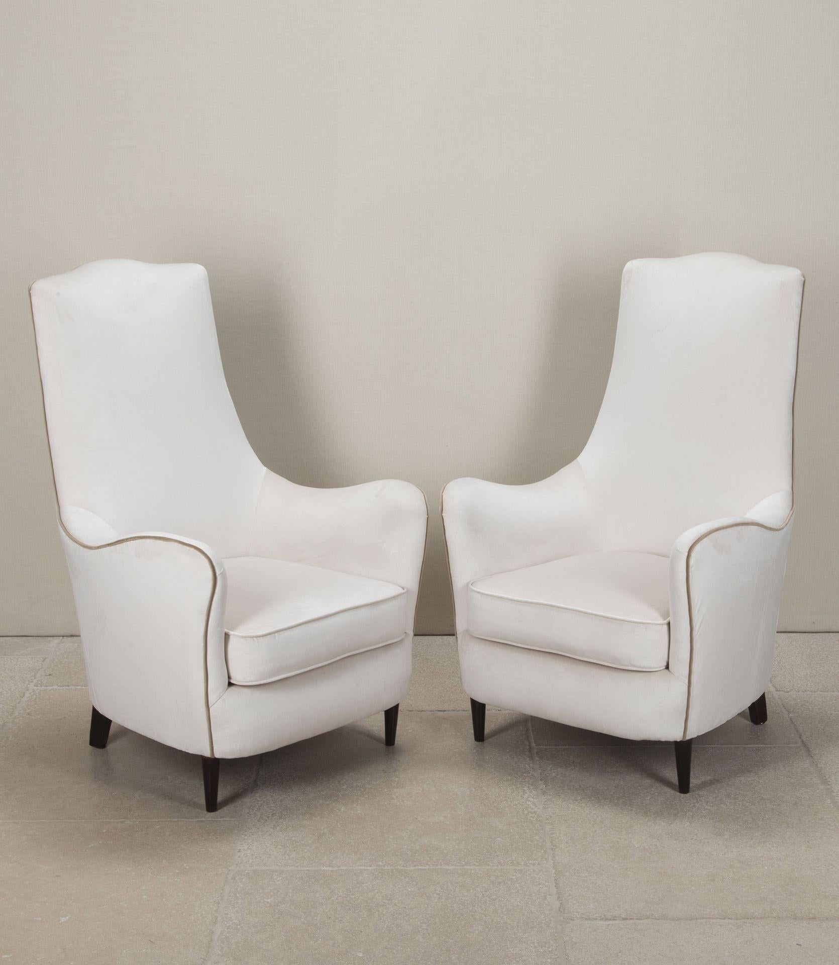 Une élégante paire de fauteuils italiens à haut dossier de forme incurvée datant du milieu du siècle dernier. 
Rembourré en velours crème avec un passepoil beige. Vers 1950.