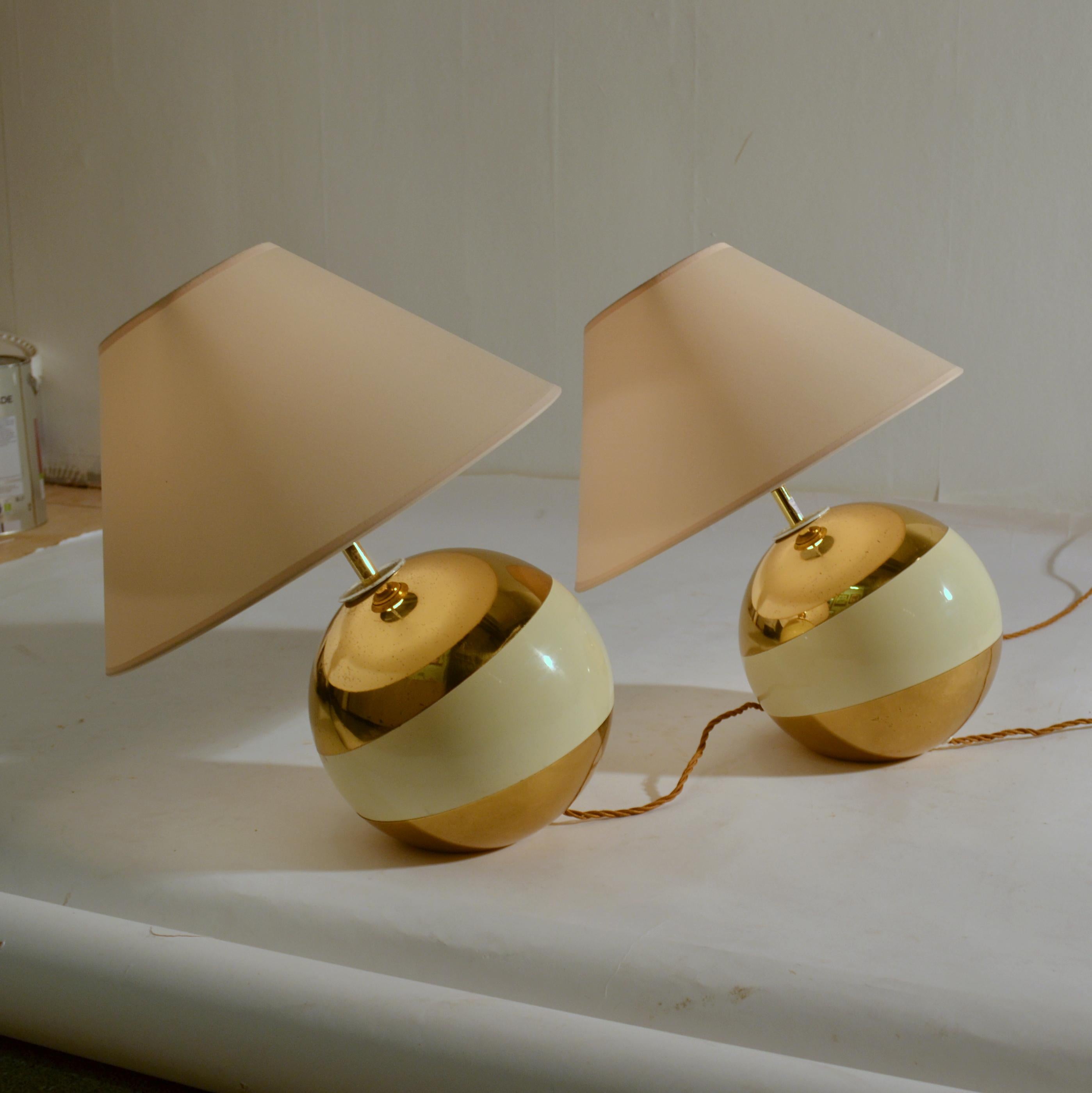 Pair of Italian 1960s leaning ball lamps spun in brass and part enameled with a cream band and cream lamp shades. They can only stand in the leaning position and are great as side table or bedside table lamps. The lampshades are new.

The leaning
