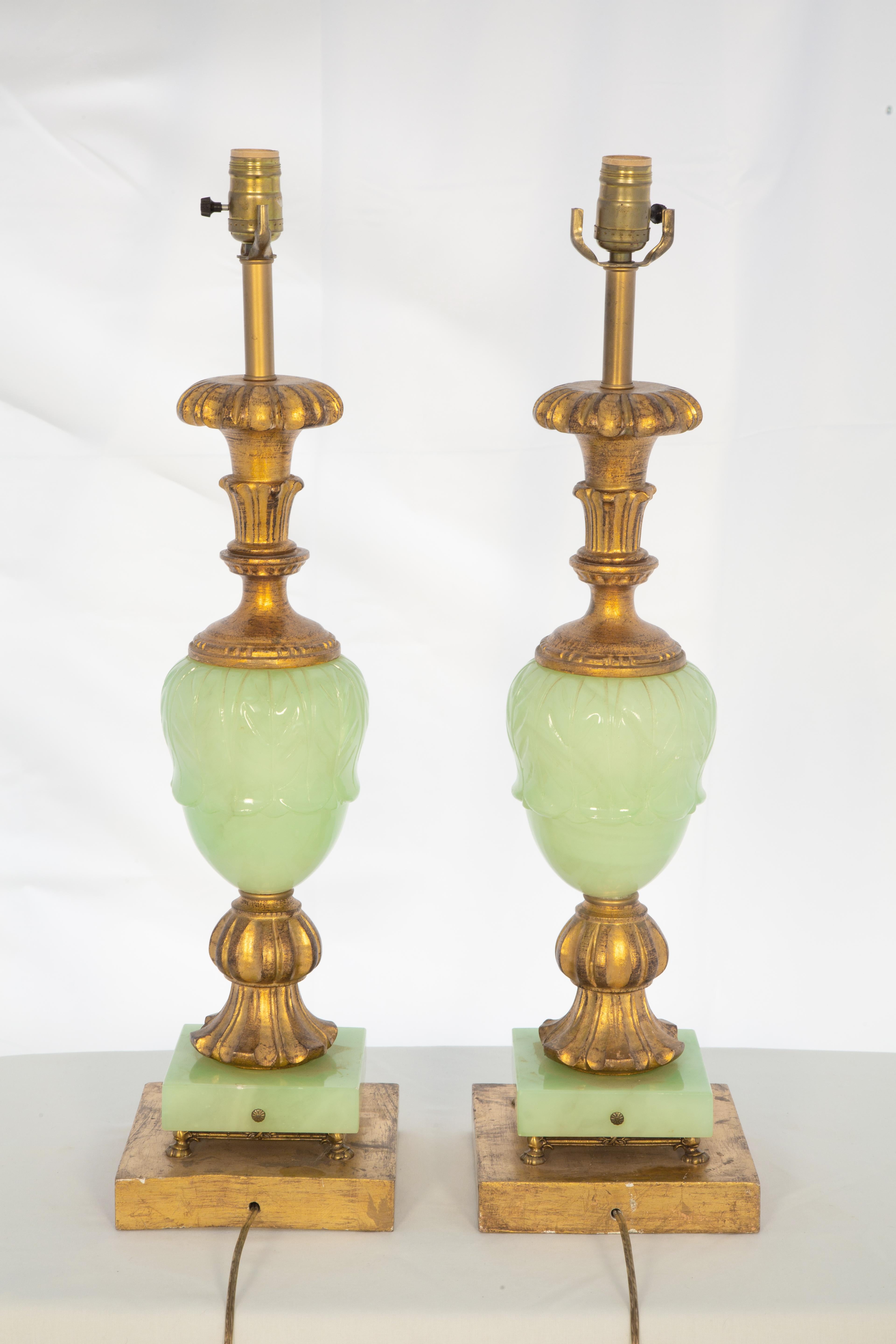 Pair of hand-carved giltwood andmint-green alabaster table lamps, each having an acorn-shaped, foliate central ornament, surmounted by a knopped cresting finial set upon a fluted foot. Four small feet of brass support the central columns, which rise