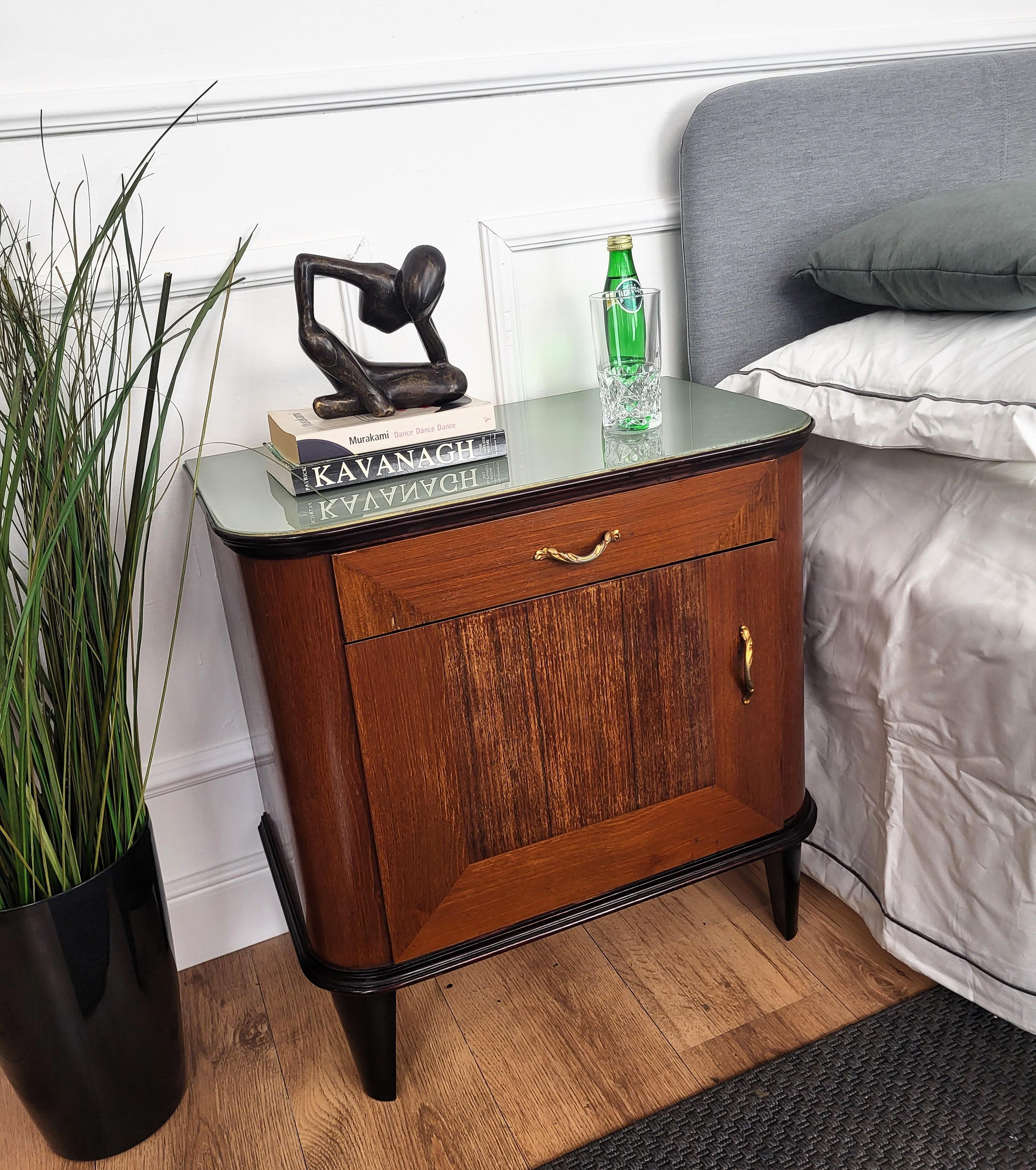 Beautiful Italian 1950s Mid-Century Modern pair of bedside tables with top drawer, wood front door and green glass top. The pieces are characterized by the wood veneer decors on the sides and doors, and by the brass details of the 4 handles. The