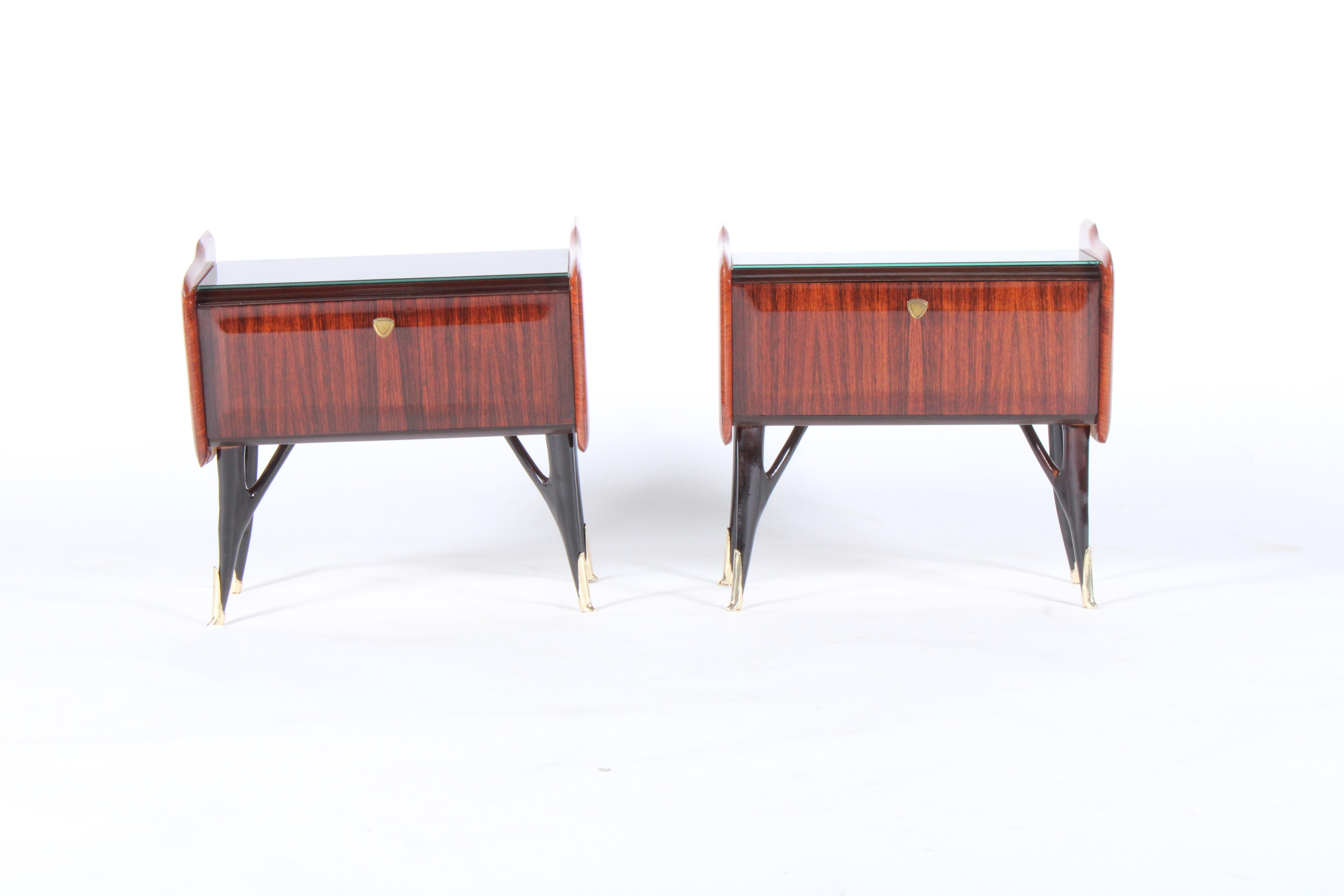 Exceptional pair of original midcentury Italian bedside cabinets in a beautiful pallisandro rosewood. Set on a sculptural ebonized base very much in the manner of Ico Parisi. This pair have an inset black glass top and have drop down door storage