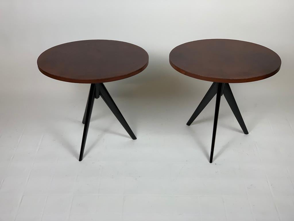 Pair of 1960's oval Italian coffee tables, three thin legs in black lacquered wood support an oval top covered in natural color leather. Due to their shape and size, these tables are suitable both for a living room near a sofa or armchairs and in