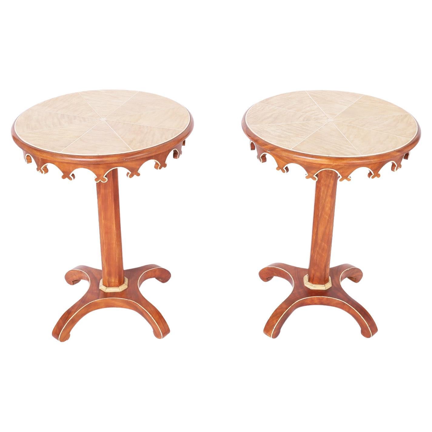 Pair of stylized neoclassic mid-century stands or tables crafted in hardwoods with a mahogany finish having round grain painted tops with scalloped skirts over a pedestal on a four legged base all outlined and highlighted with blonde wood.
