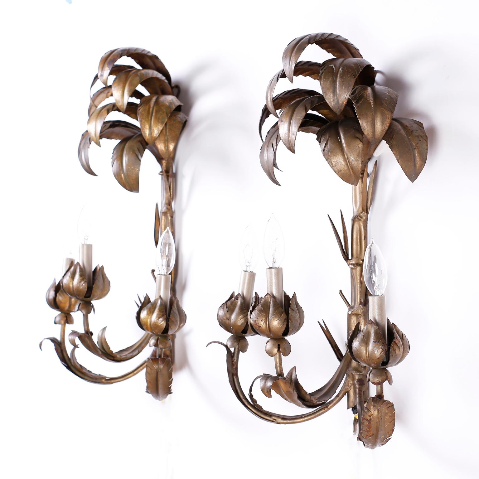 Chic pair of wall sconces crafted in metal with stylized palm tops, faux bamboo trunks and three arms with leaf candle cups, all with a contrived antique finish.