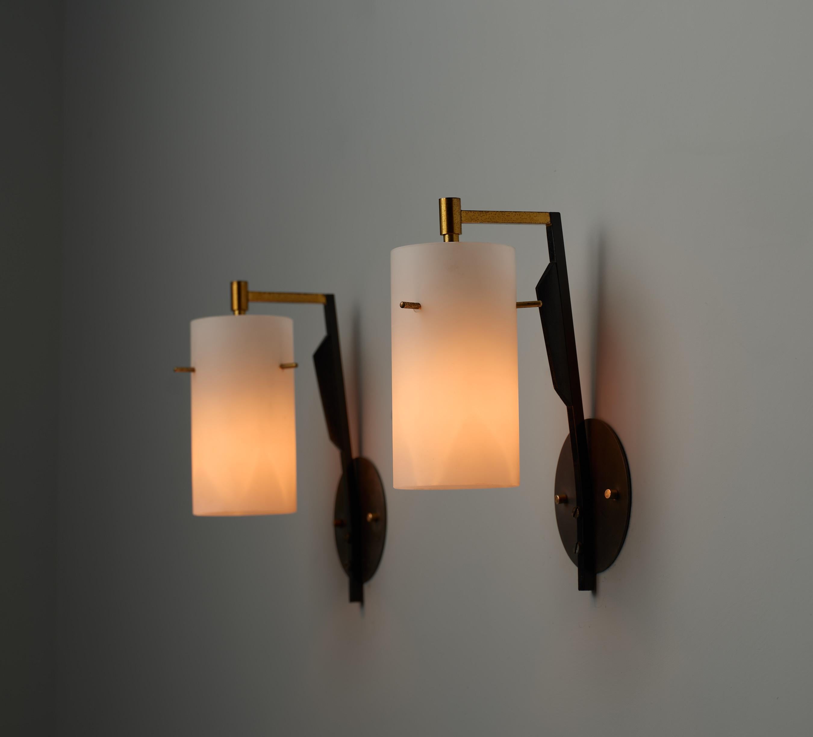 Pair of 1950s Italian sconces attributed to Stilnovo. The frame is made of brass and black lacquered wood, with a portion of the brass also lacquered in black. Each sconce, or wall lamp, features a cylindrical opaline glass shade. The brass parts