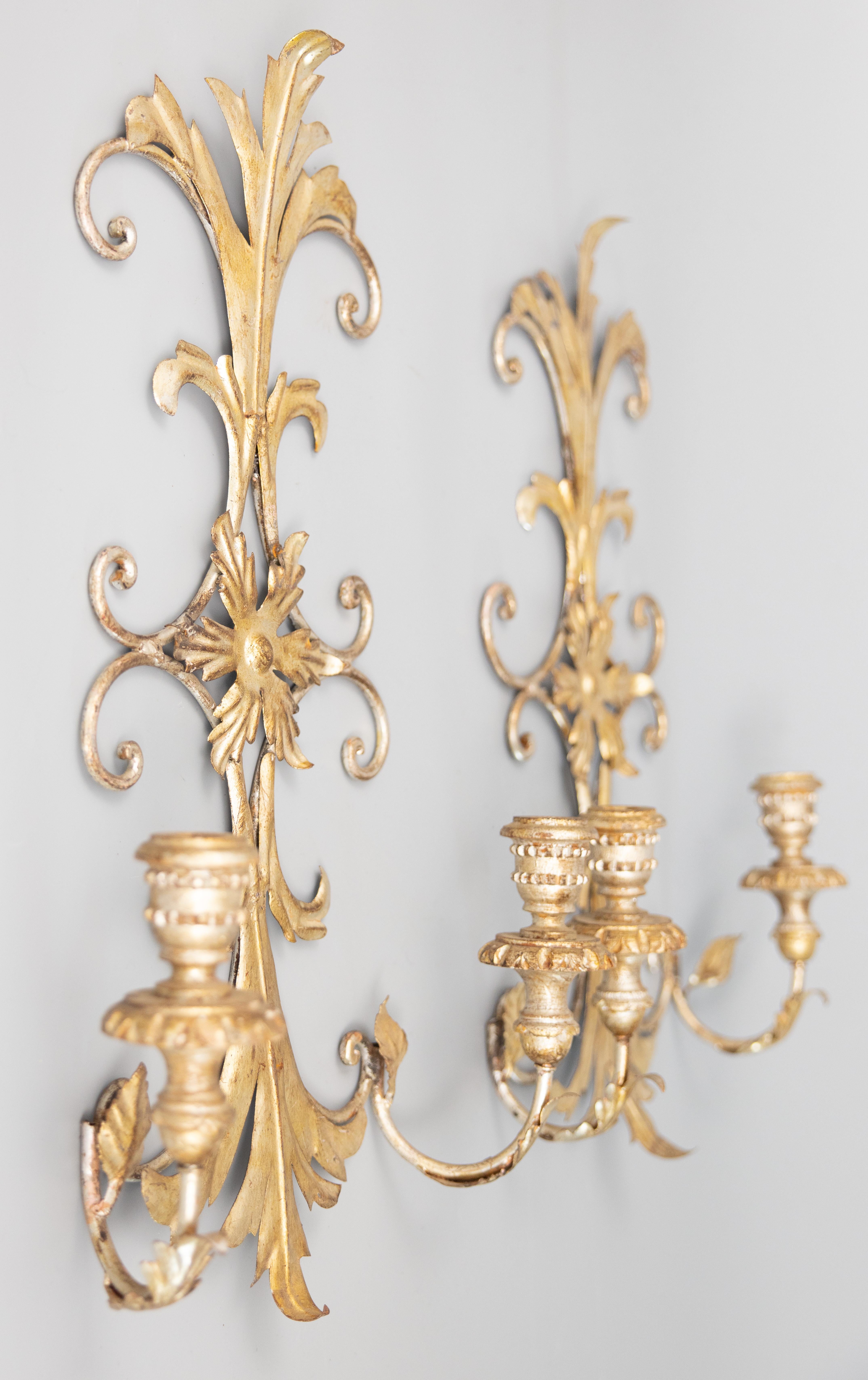 A stunning pair of Mid-Century Italian silver gilt tole two arm candle wall sconces. These gorgeous sconces are decorated with flowers and scrolling leaves with giltwood candle holders in a lovely silvered patina. They would make a fabulous addition