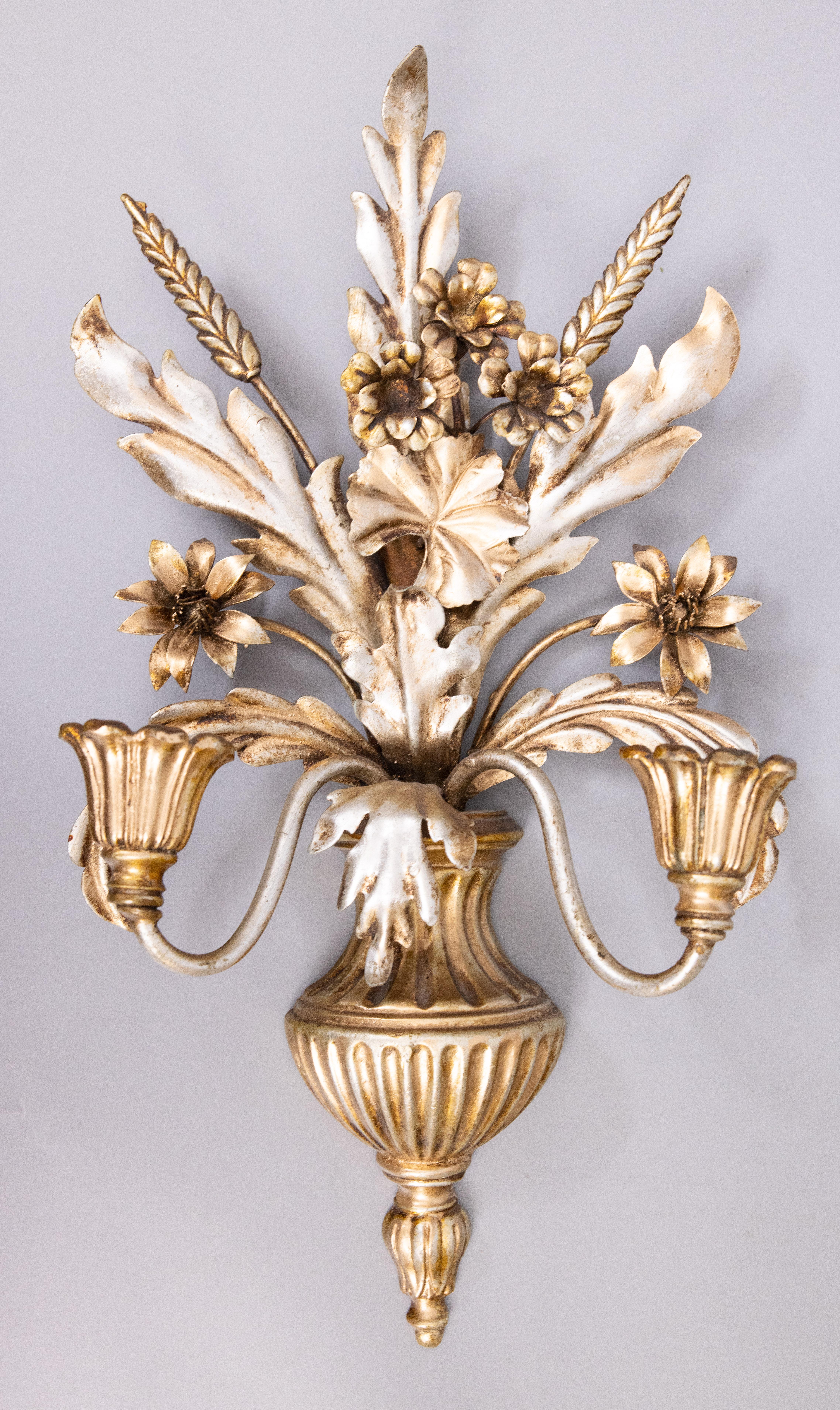 A stunning pair of Mid-Century Italian silver and gold gilt tole two arm candle wall sconces. These gorgeous sconces are decorated with flowers, leaves, and wheat in a lovely silvered gilt patina. They would make a fabulous addition to any
