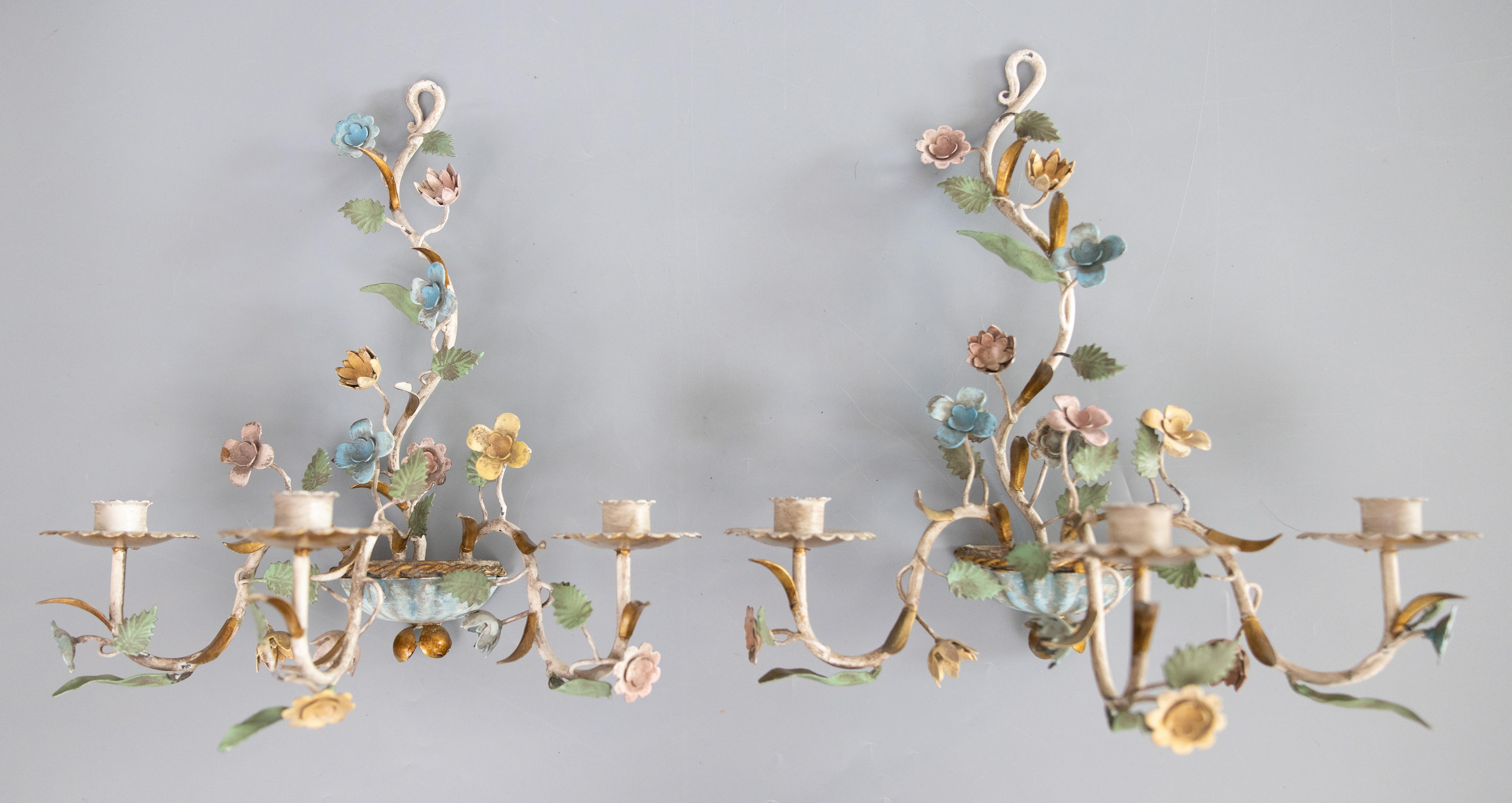 Preciosa pareja de candelabros de dos brazos de tole italiano vintage con flores silvestres pintadas a mano en tonos pastel, hojas verdes en espiral y detalles dorados, hacia 1950. Conservan su superficie original y una maravillosa pátina