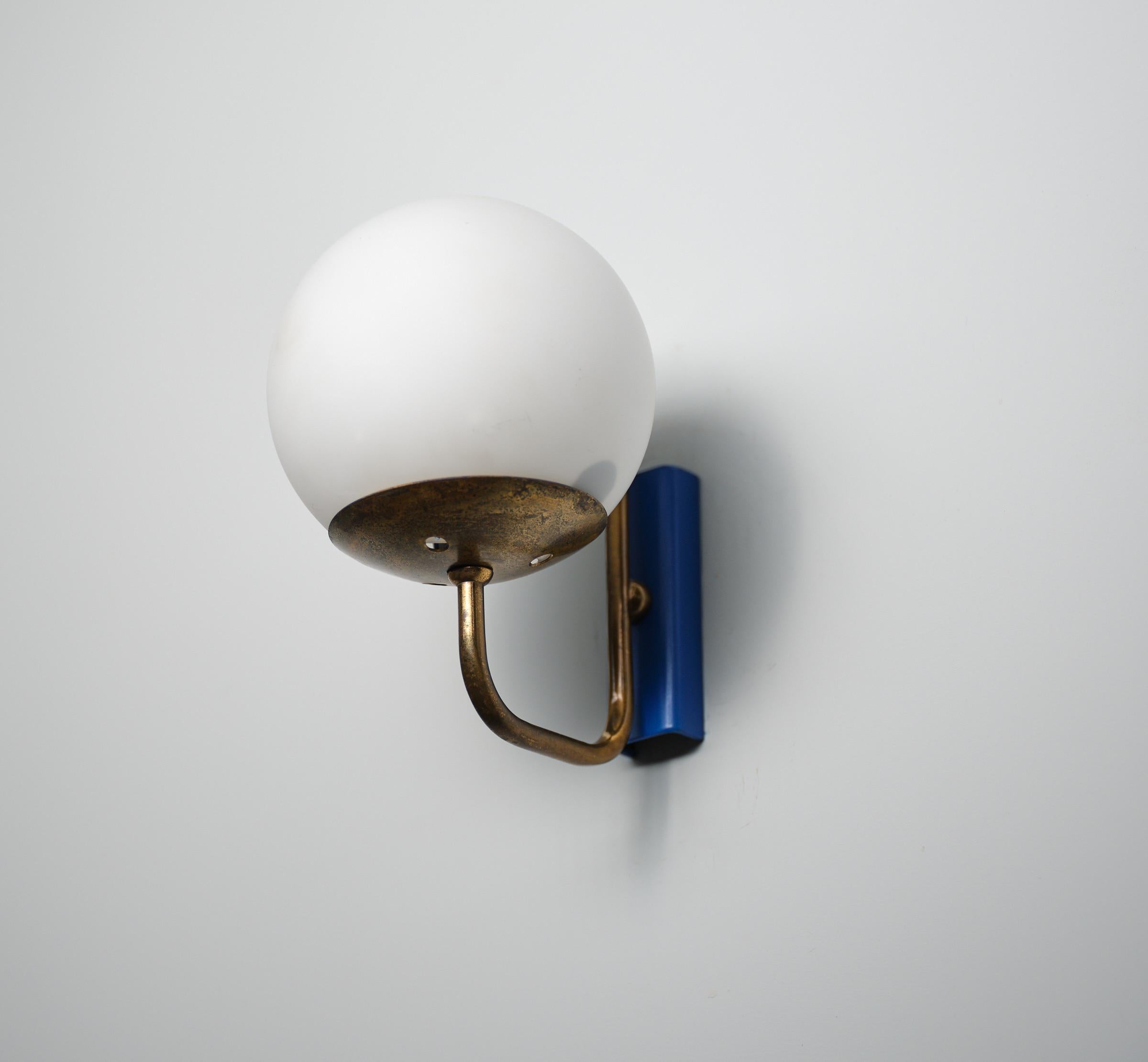 This elegant pair of Italian wall sconces from the 1950s exemplifies the sophistication and refined aesthetics of mid-century design. Each sconce features a vibrant blue enameled steel backplate that provides a stunning contrast to the warm golden