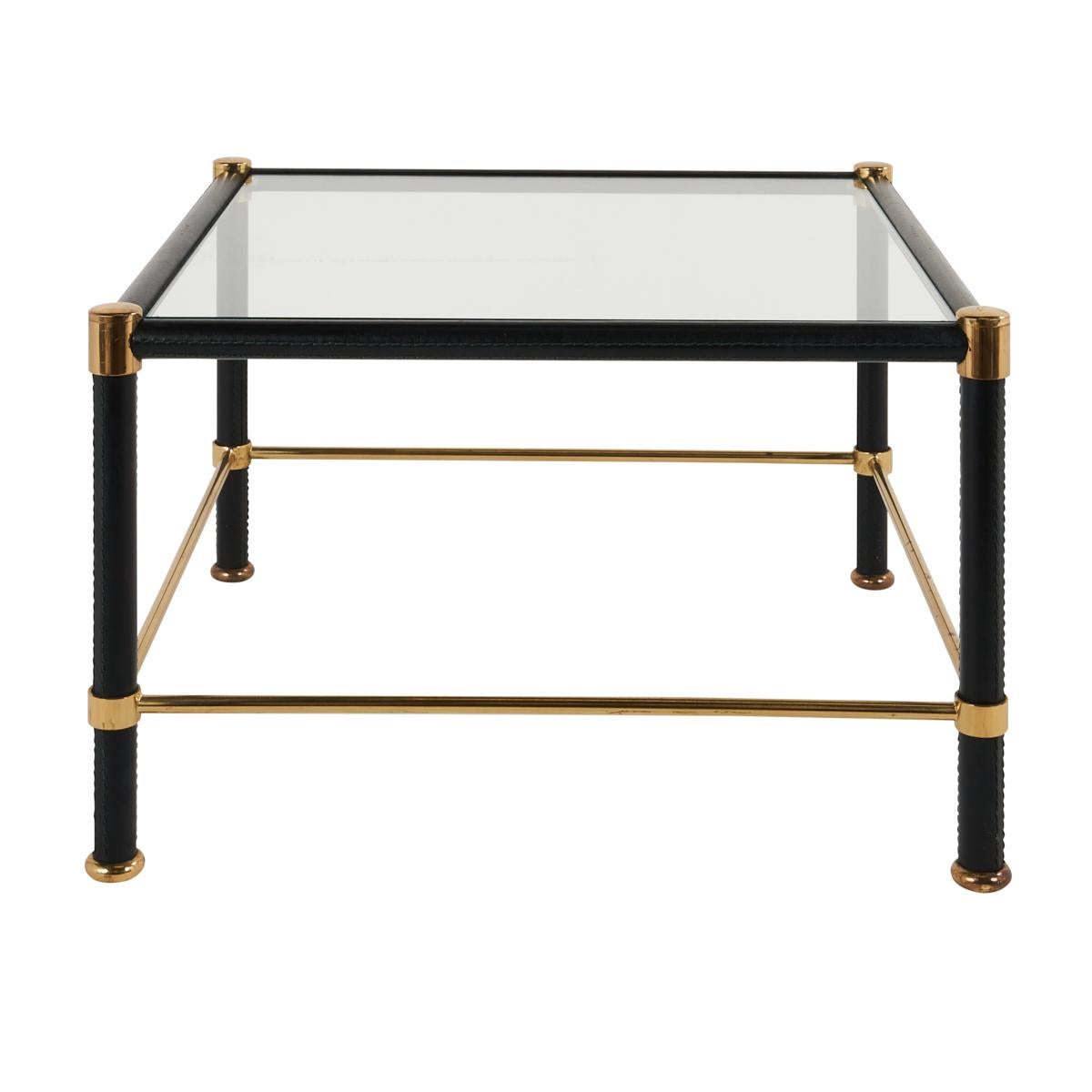 These handsome French glass-top side tables are wrapped in leather with green stitching and brass accents, in the style of Jacques Adnet. Wonderfully lithe, infinitely versatile and ever chic, this two-piece set adds sophistication and luxury to