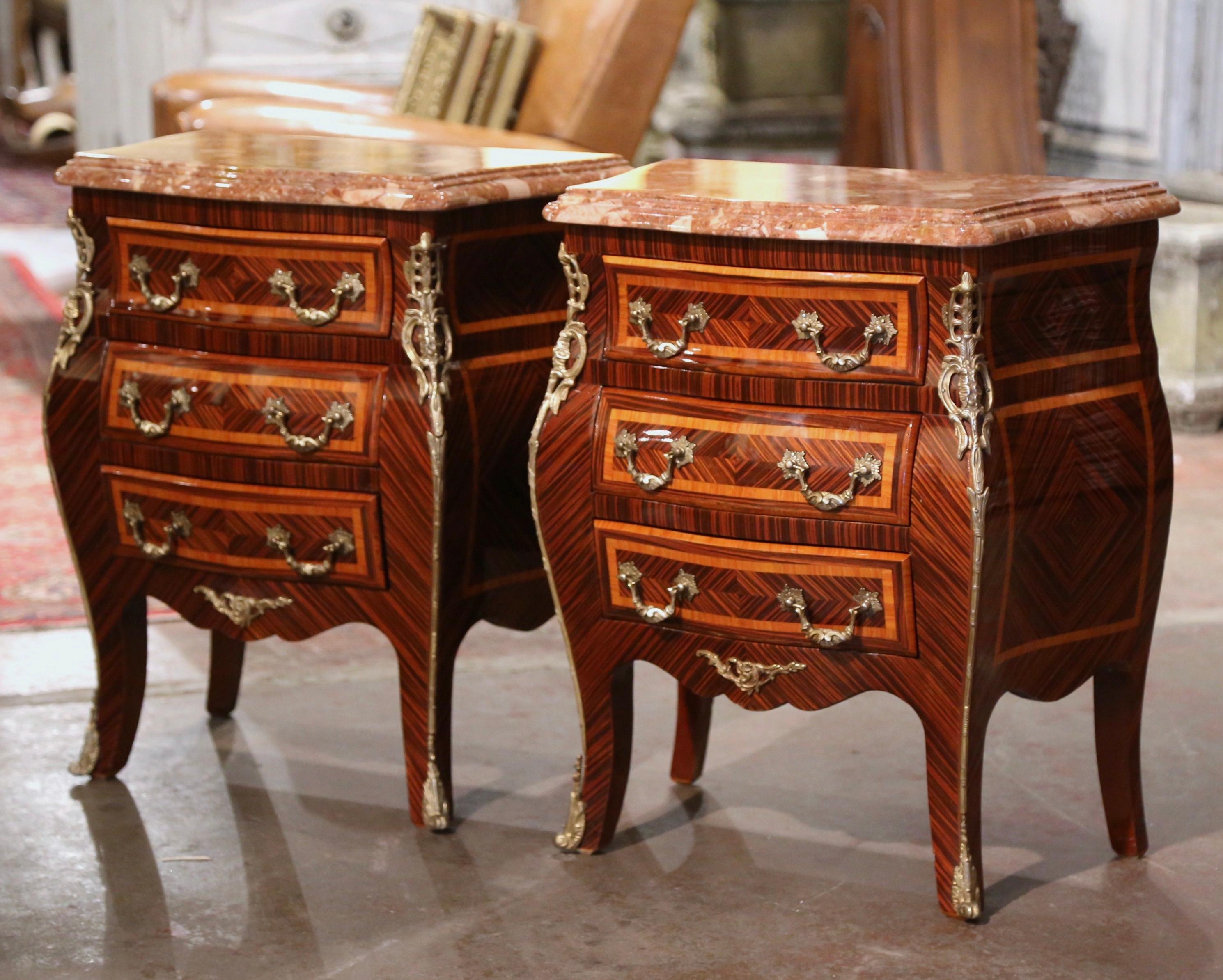 These elegant three-drawer bedside tables were created in France, circa 1980. Bombe in shape on all three sides, each chest stands on cabriole legs ending with bronze sabot feet over a scalloped apron embellished with a brass mount; the sides with