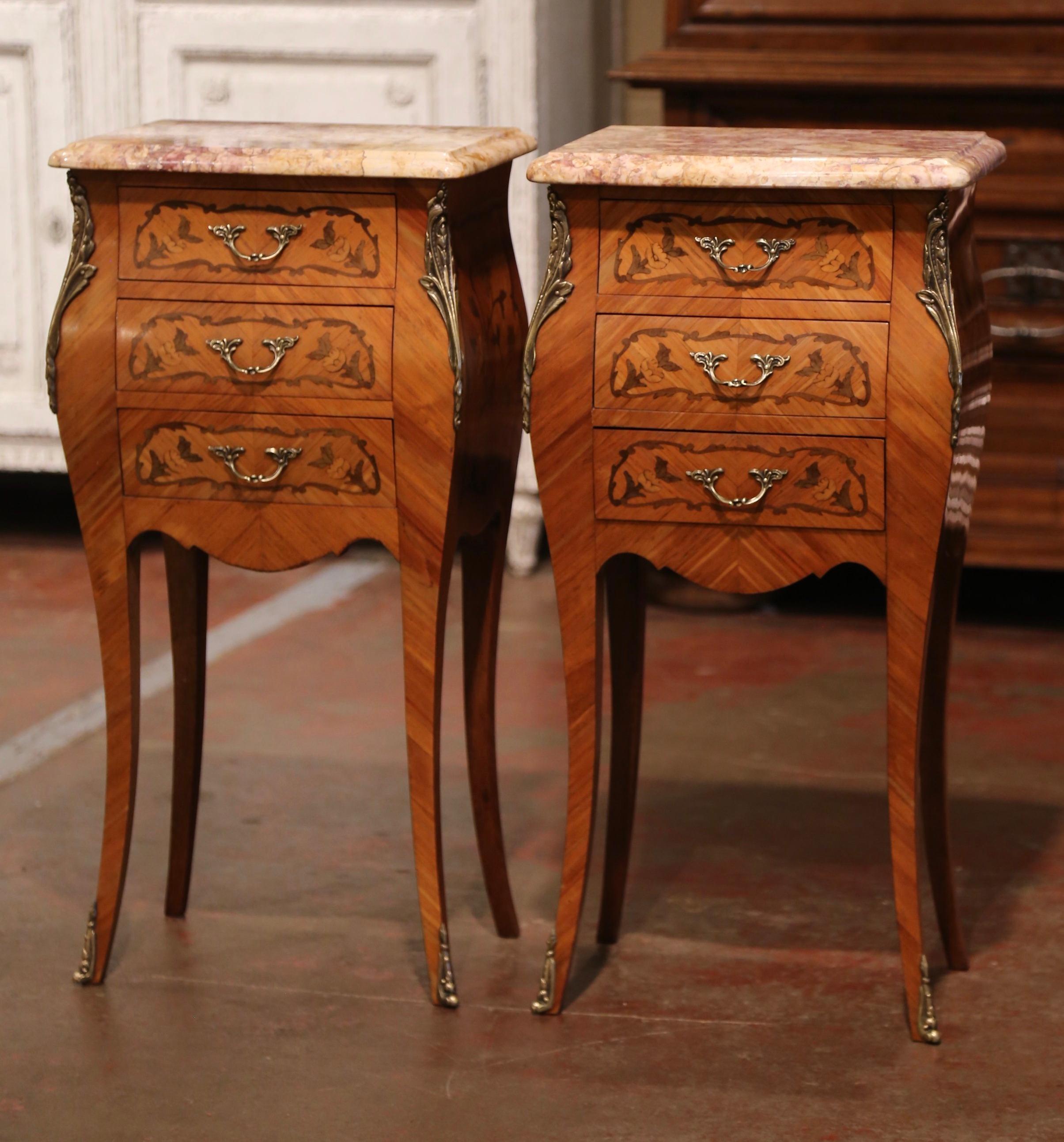 These elegant nightstands were created in France, circa 1970. Bombe in shape on all three sides, each mahogany cabinet stands on cabriole legs ending with gilt metal mounts, over a scalloped apron. Both curved sides are decorated with inlaid floral