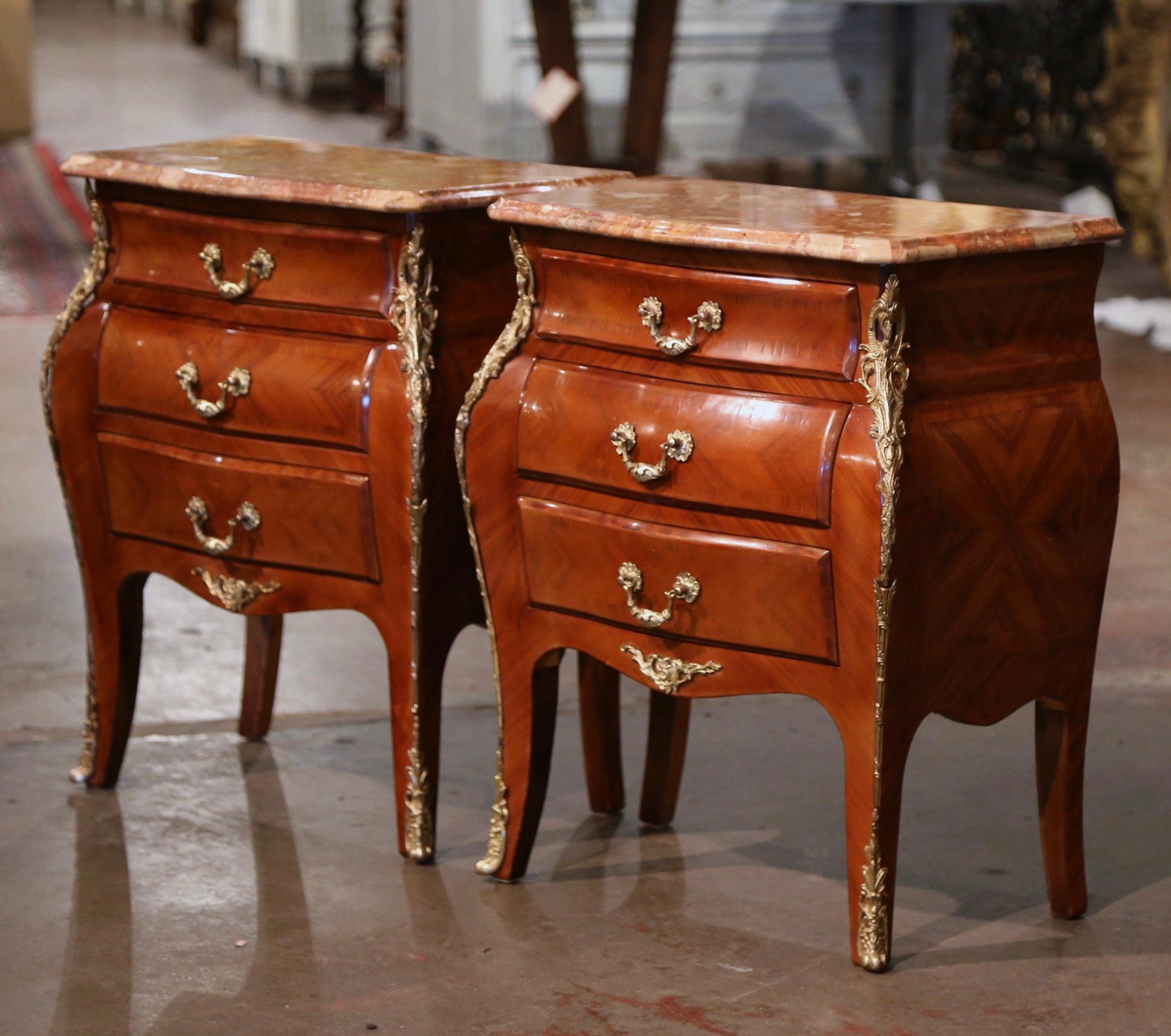 These elegant three-drawer bedside tables were created in France, circa 1970. Bombe in shape on all three sides, each chest stands on cabriole legs ending with bronze sabot feet over a scalloped apron embellished with a brass mount; the sides with