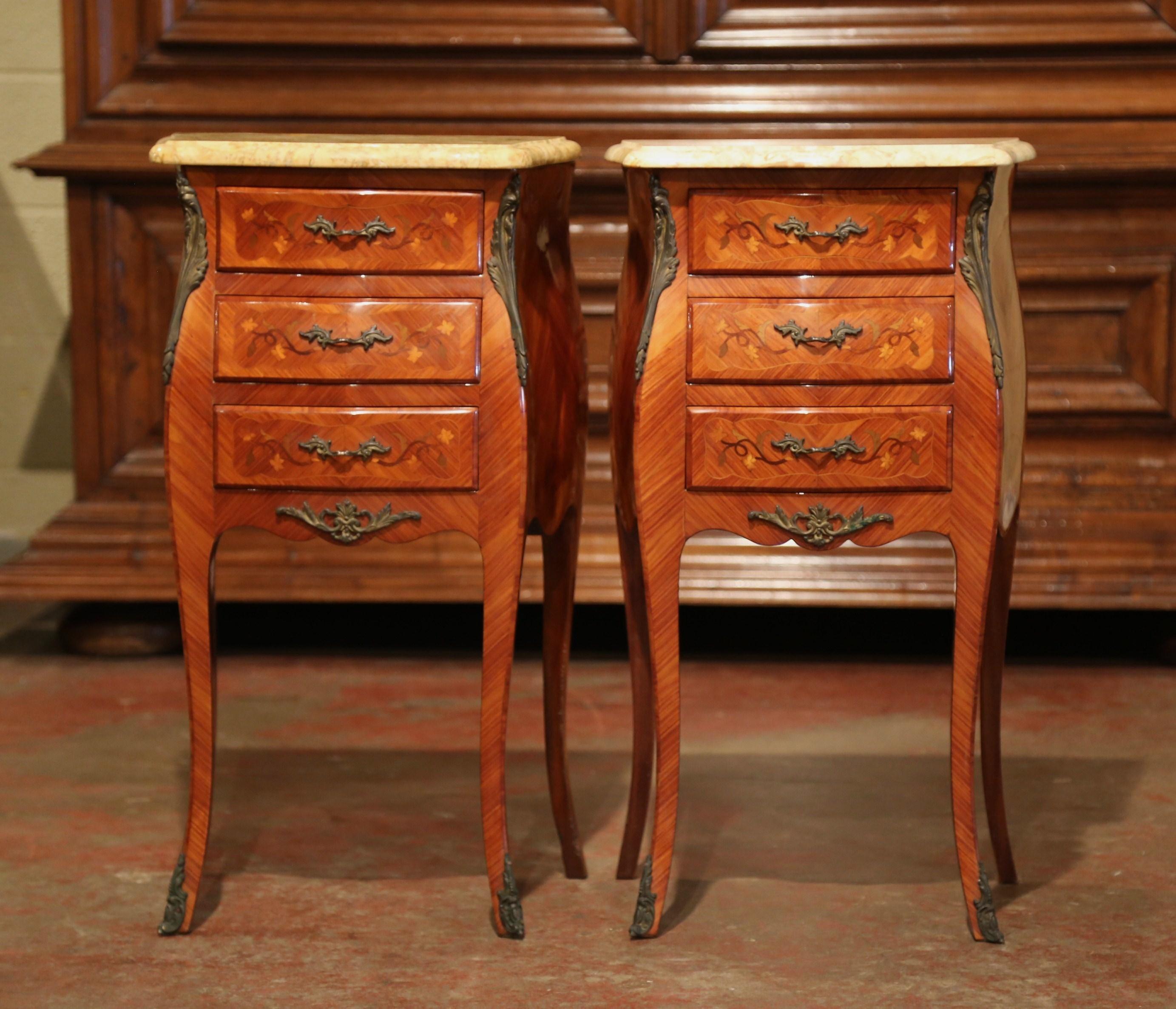 These elegant bedside tables were created in France, circa 1950. Bombe in shape on all three sides, the fruitwood cabinets stand on tall cabriole legs with decorative brass sabot feet; both sides with serpentine shape have an inlay veneer chevron