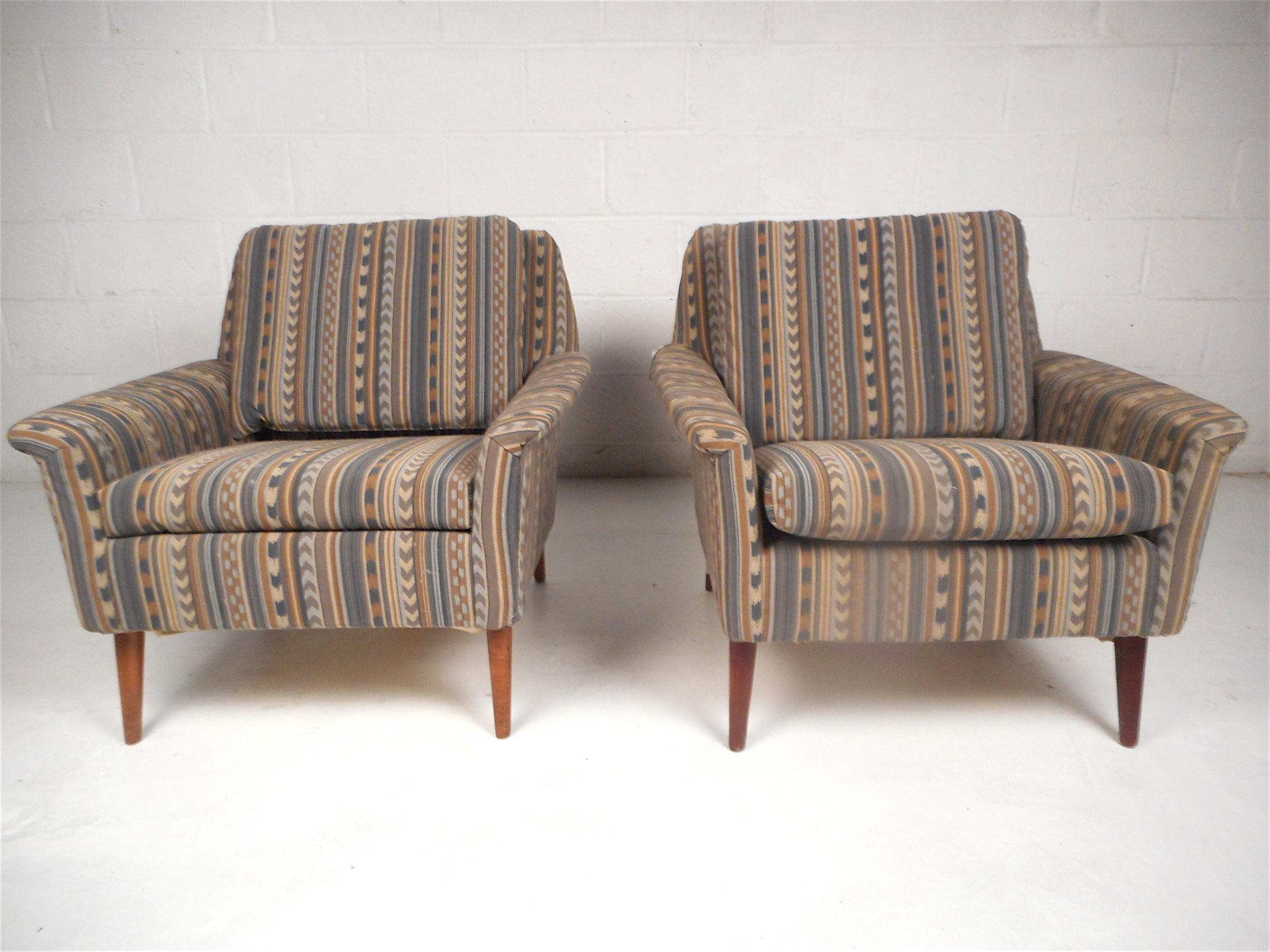 Stylish pair of midcentury lounge chairs. Spacious and comfortable seating with sloped backrests. Sturdy and sleek tapered wooden legs. Covered in a vintage western tapestry style upholstery. Beautiful pair of midcentury chairs sure to impress in