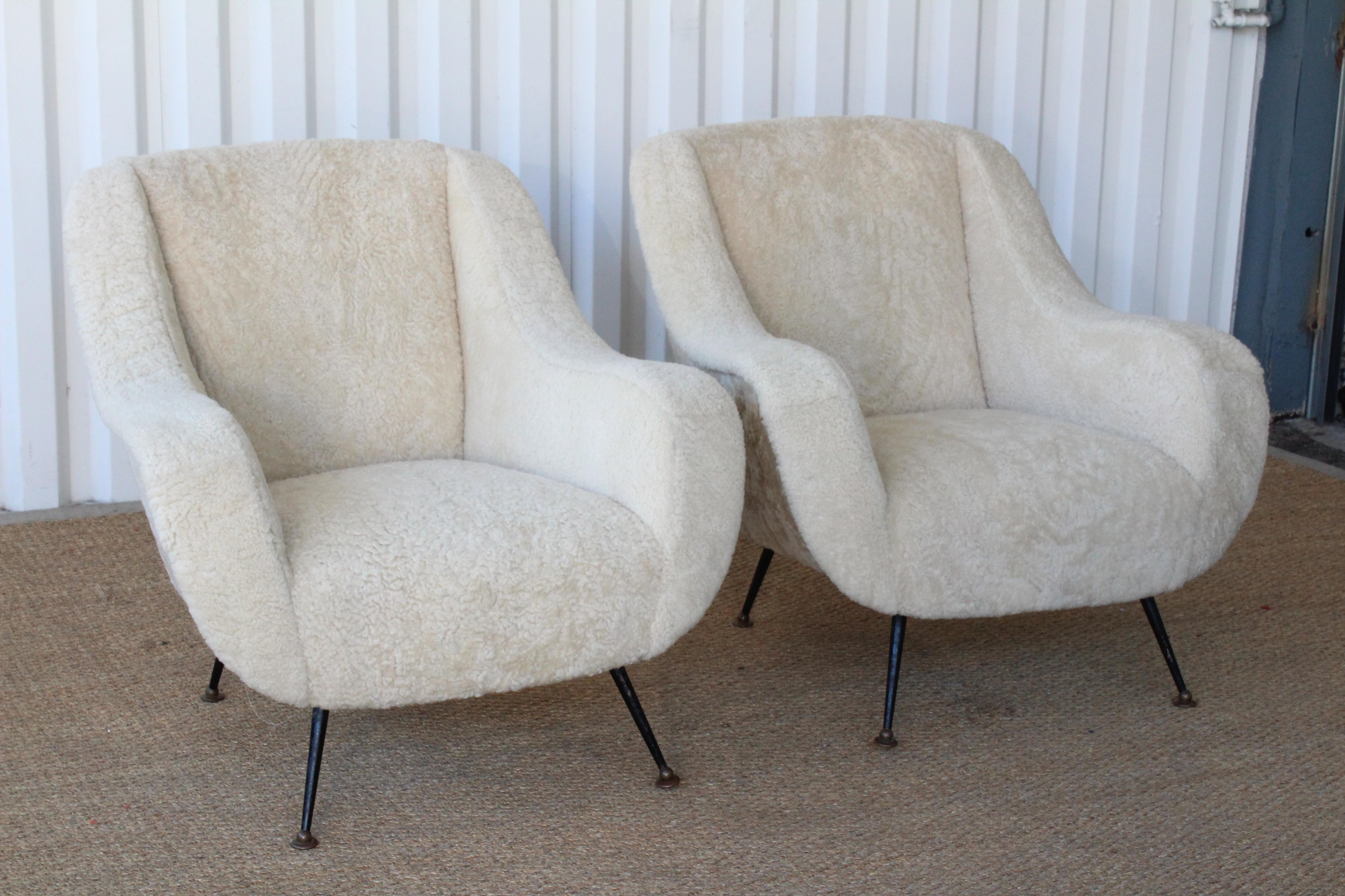 Pair of vintage mid-century lounge chairs, Italy, 1950s. Newly upholstered in off white sheepskin hides. The pair are super comfortable and in excellent condition. The legs are iron with brass pivoting sabots- and retain their age appropriate