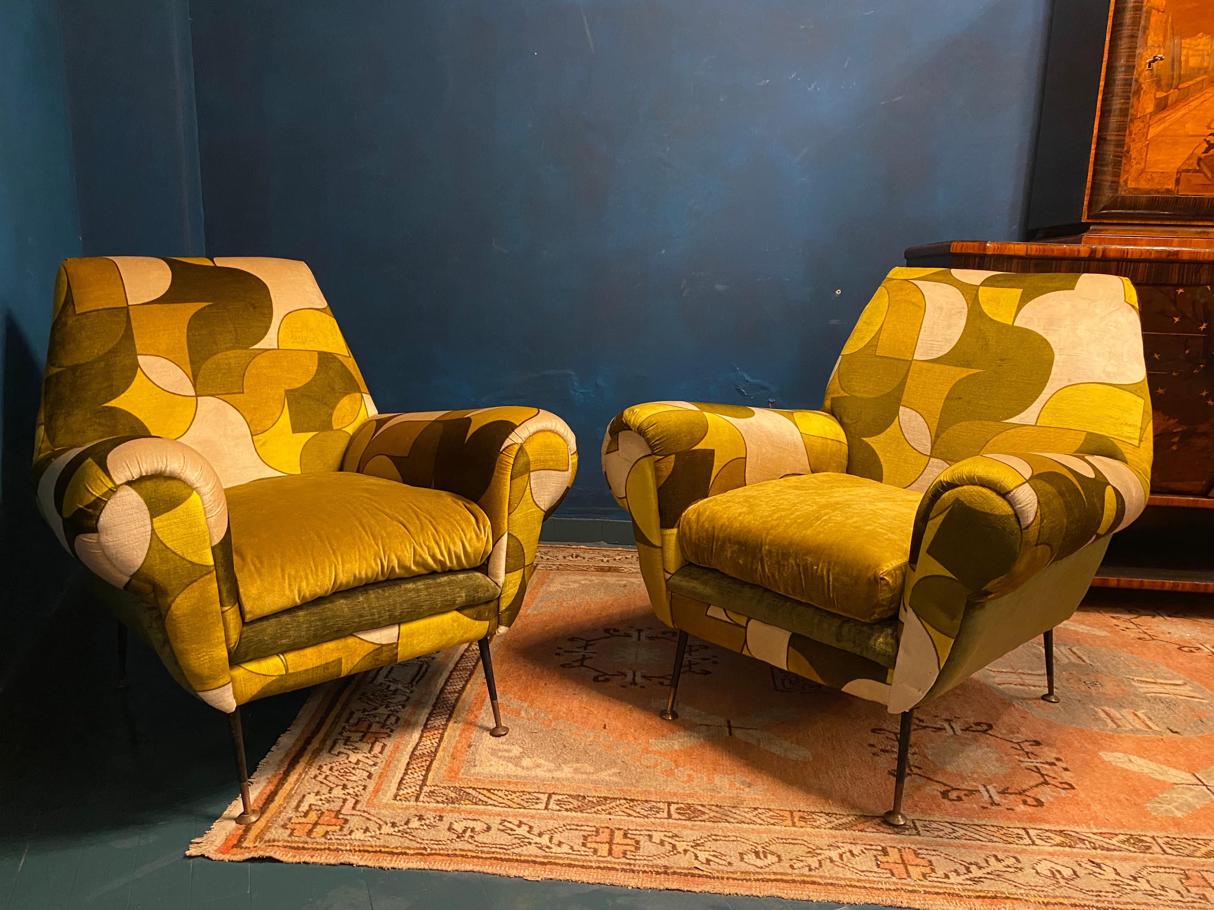 Very comfortable pair of armchairs with scrolled hand holds by Gigi Radice for Minotti. 
 Soft and beautiful original vintage multicolor velvet upholstery. The conical legs are black enameled steel encased in brass-plated feet in original