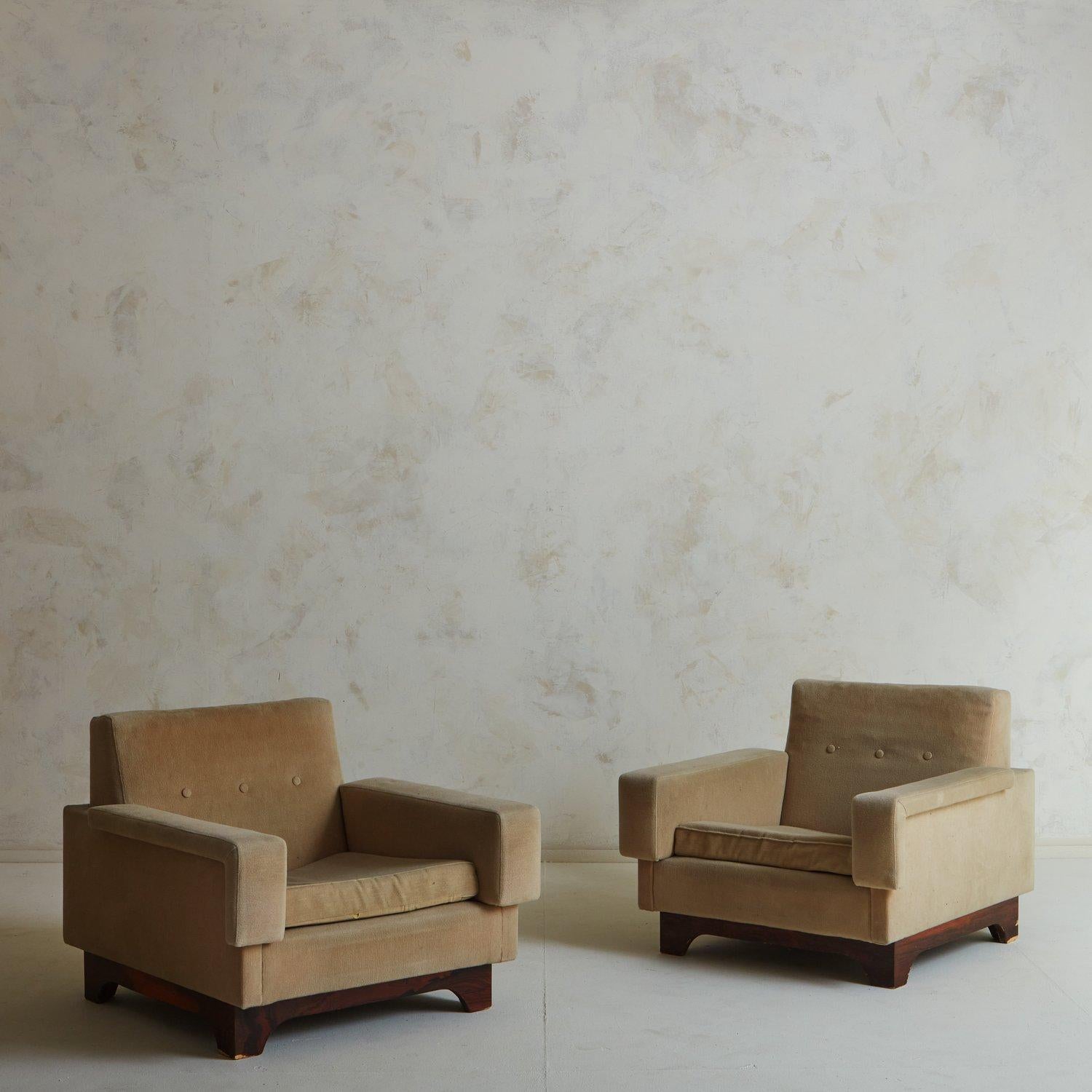 A stately pair of mid-century lounge chairs by Saporiti Italia. These chairs have carved wood bases with beautiful graining and feature sleek, angular lines. They retain their original taupe upholstery with three buttons on each seat back.