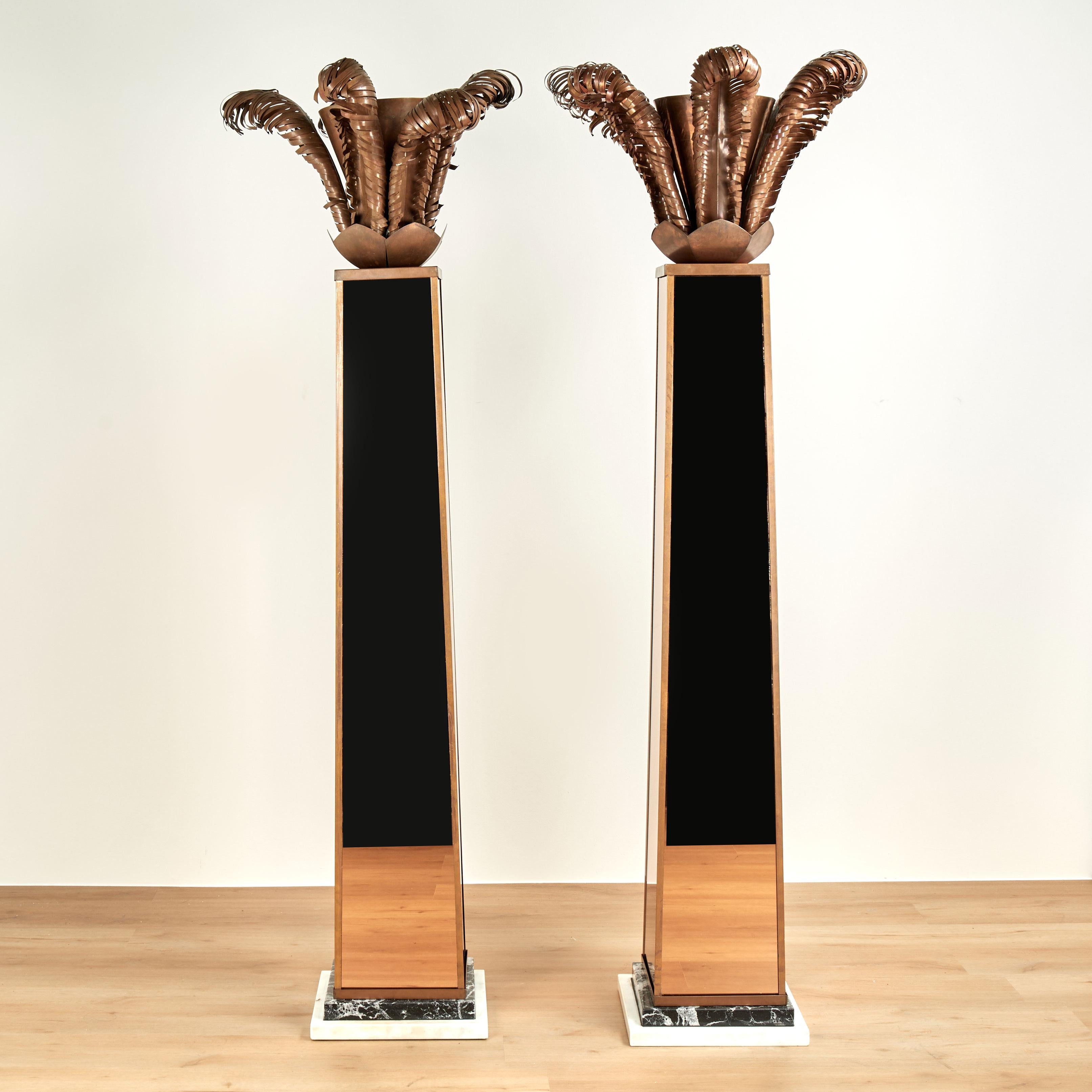 Rare and remarkable pair of vintage torchiere floor lamps crafted with copper shades decorated with copper stylized palm leaves over columns with copper tinted mirrors set on black and white marble plinths.