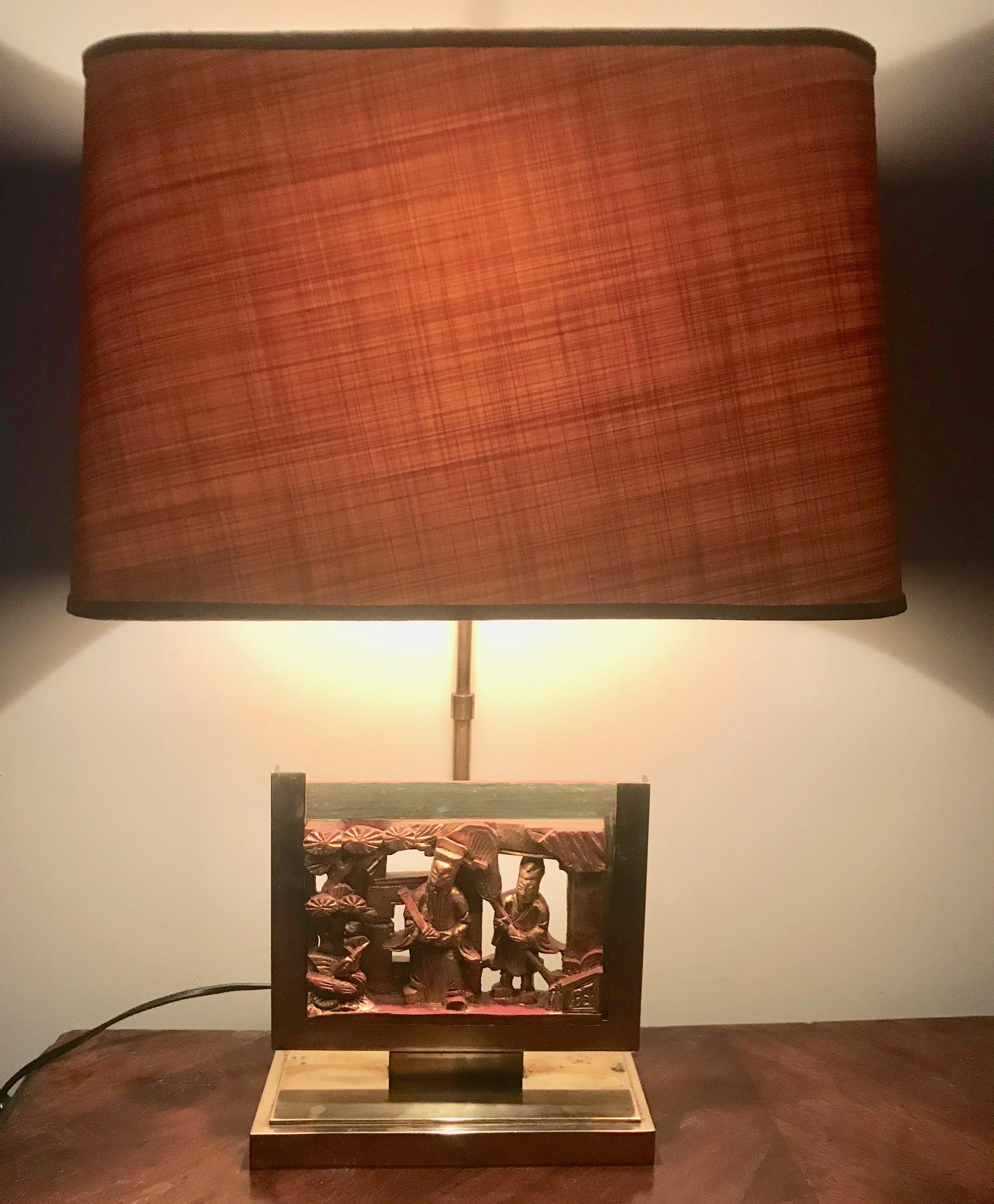 A pair of circa 1960 French Mid-Century Modern brass table lamps featuring two 19th century Chinese carved wood panels. The panels are unique and each retains traces of paint and gold leaf. The lamp shades are original (custom made for the lamps) in