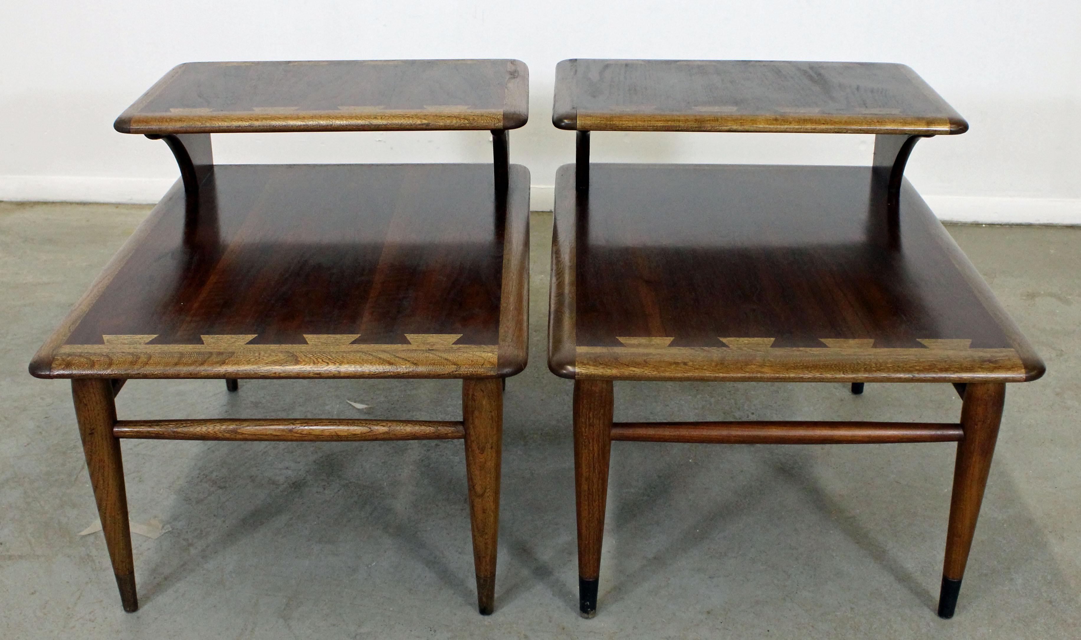 Offered is a pair of mid century modern end tables from the Lane 'Acclaim' collection, designed by Andre Bus. They have the signature dovetailed design, two tiers, and tapered legs with an oak edge with a walnut top and walnut legs. They are in