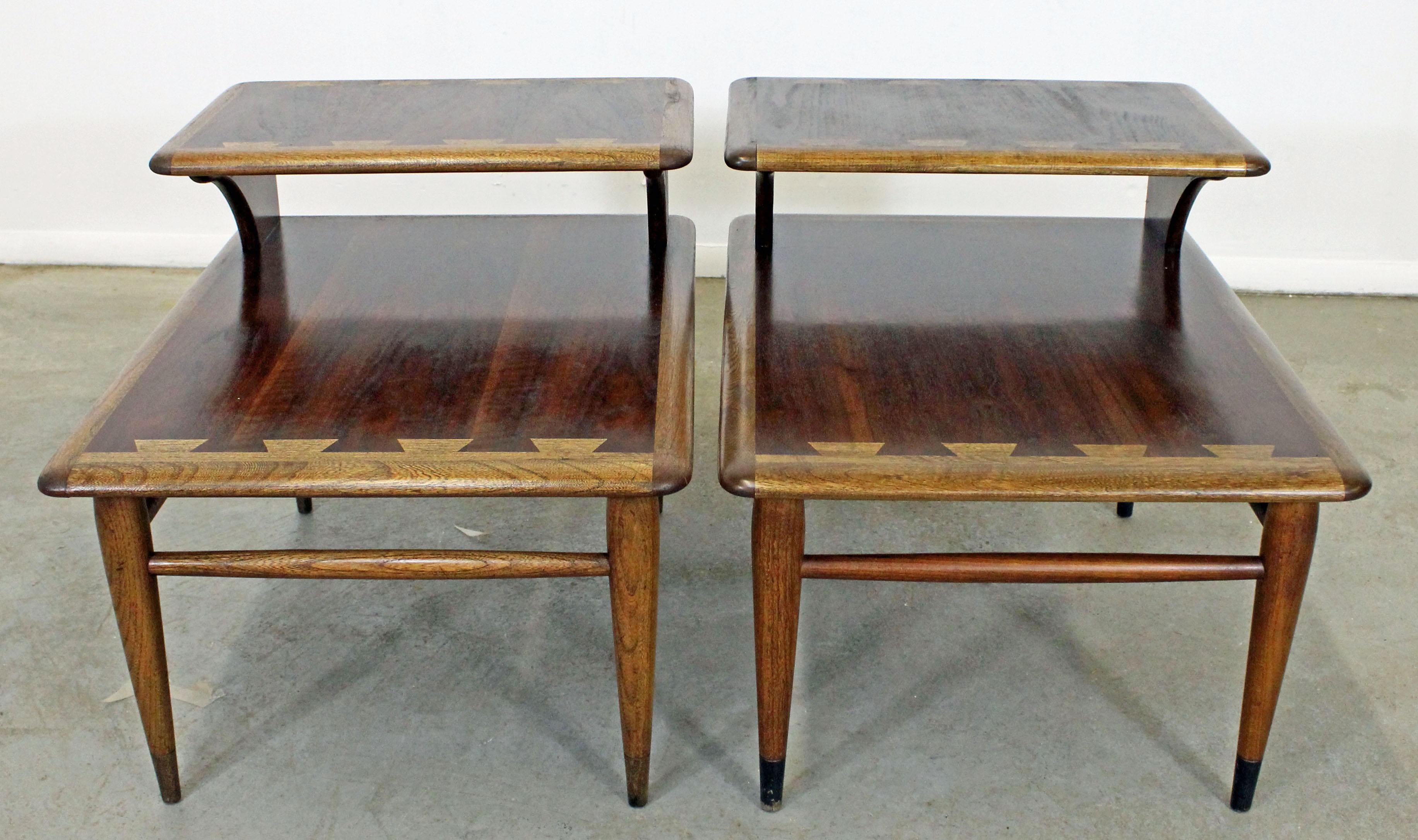 Offered is a pair of Mid-Century Modern end tables from the Lane 'Acclaim' collection, designed by Andre Bus. They have the signature dovetailed design, two tiers, and tapered legs with an oak edge with a walnut top and walnut legs. They are in