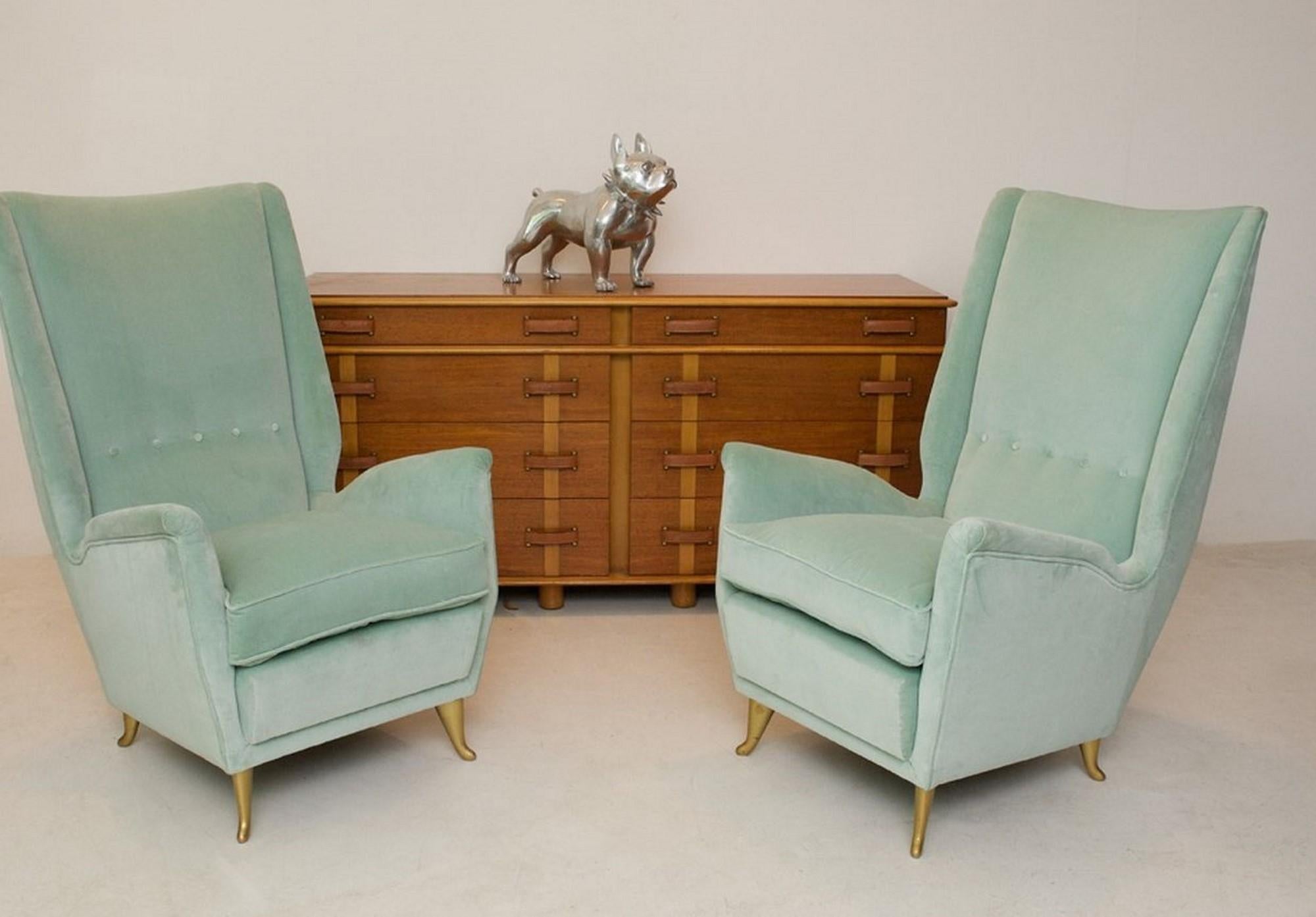 Pair of high backed stylish wing chairs with brass shaped feet. Reupholstered in quality peppermint green velvet. These chairs are an iconic design statement of the 1950s. The chairs are very comfortable and would equally be at home in a living room