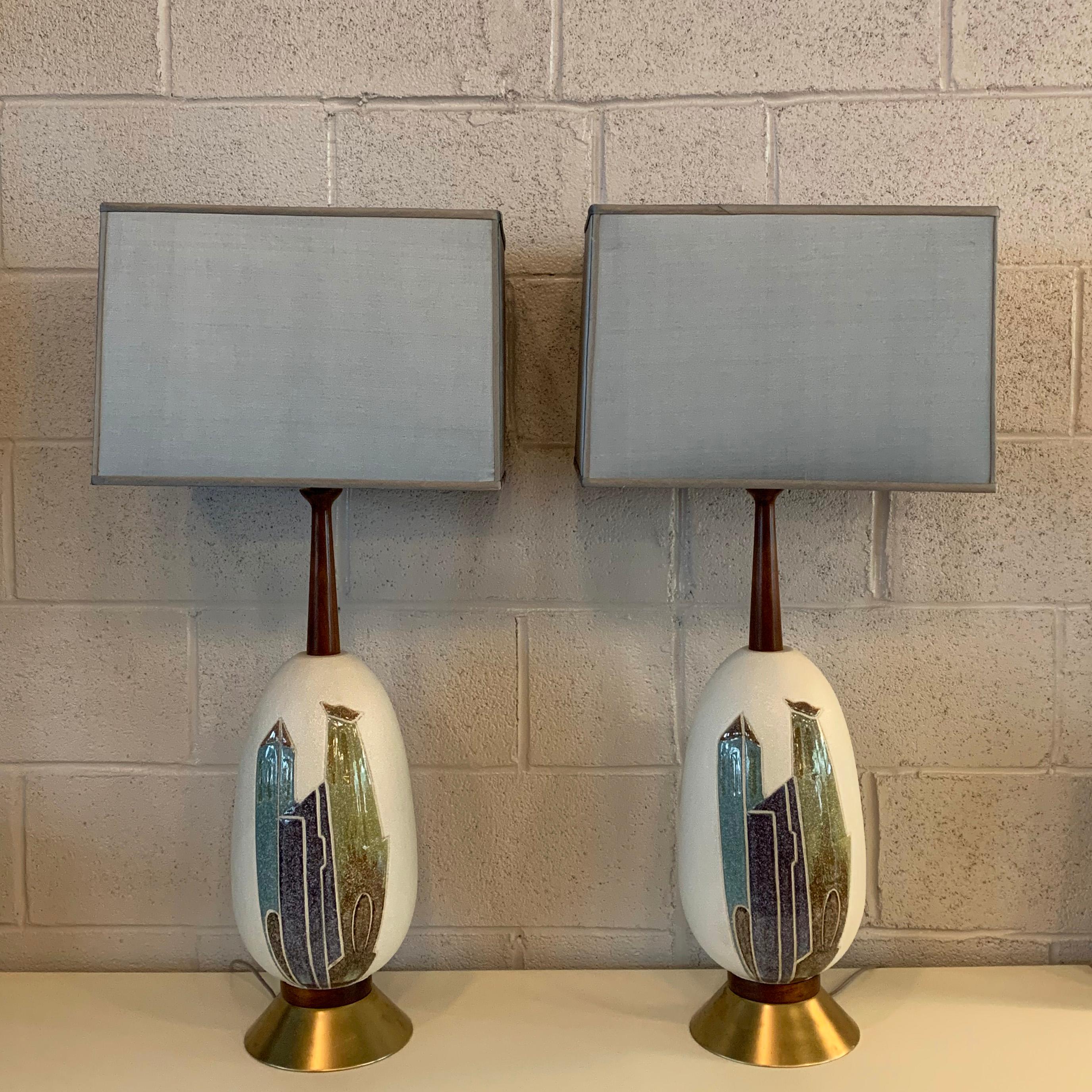 Pair of Mid-Century Modern, art pottery table lamps feature ceramic, walnut and metal bases with light blue square silk shades. The overall height of the lamps is 35 inches. The height to the socket is 27 inches. The shade dimensions are 16 width x