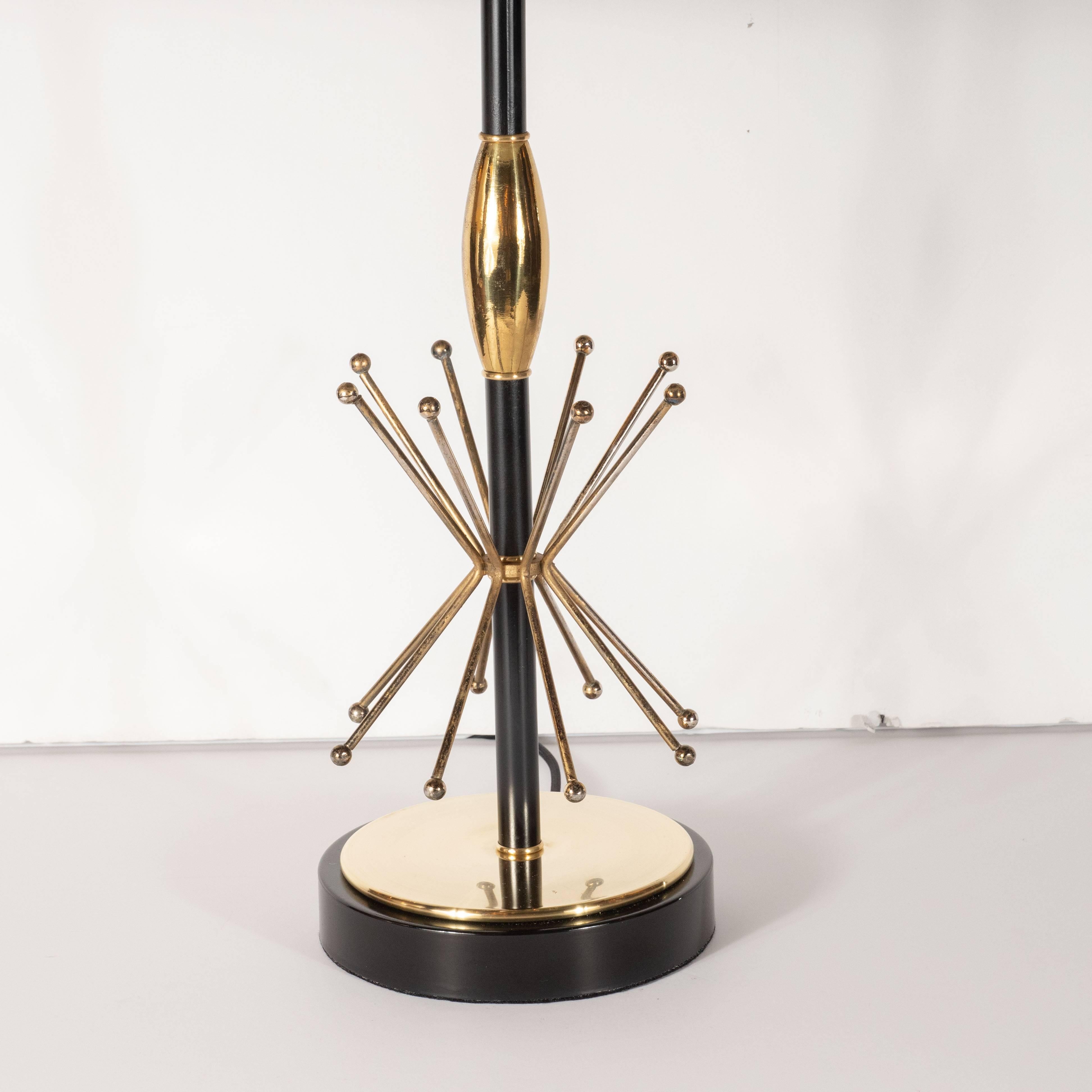 This dramatic and graphic pair of table lamps were realized in the United States, circa 1950. They feature circular black enamel bases with lustrous brass centers. A black enamel rod ascends from the center, wrapped in the middle with a protuberant