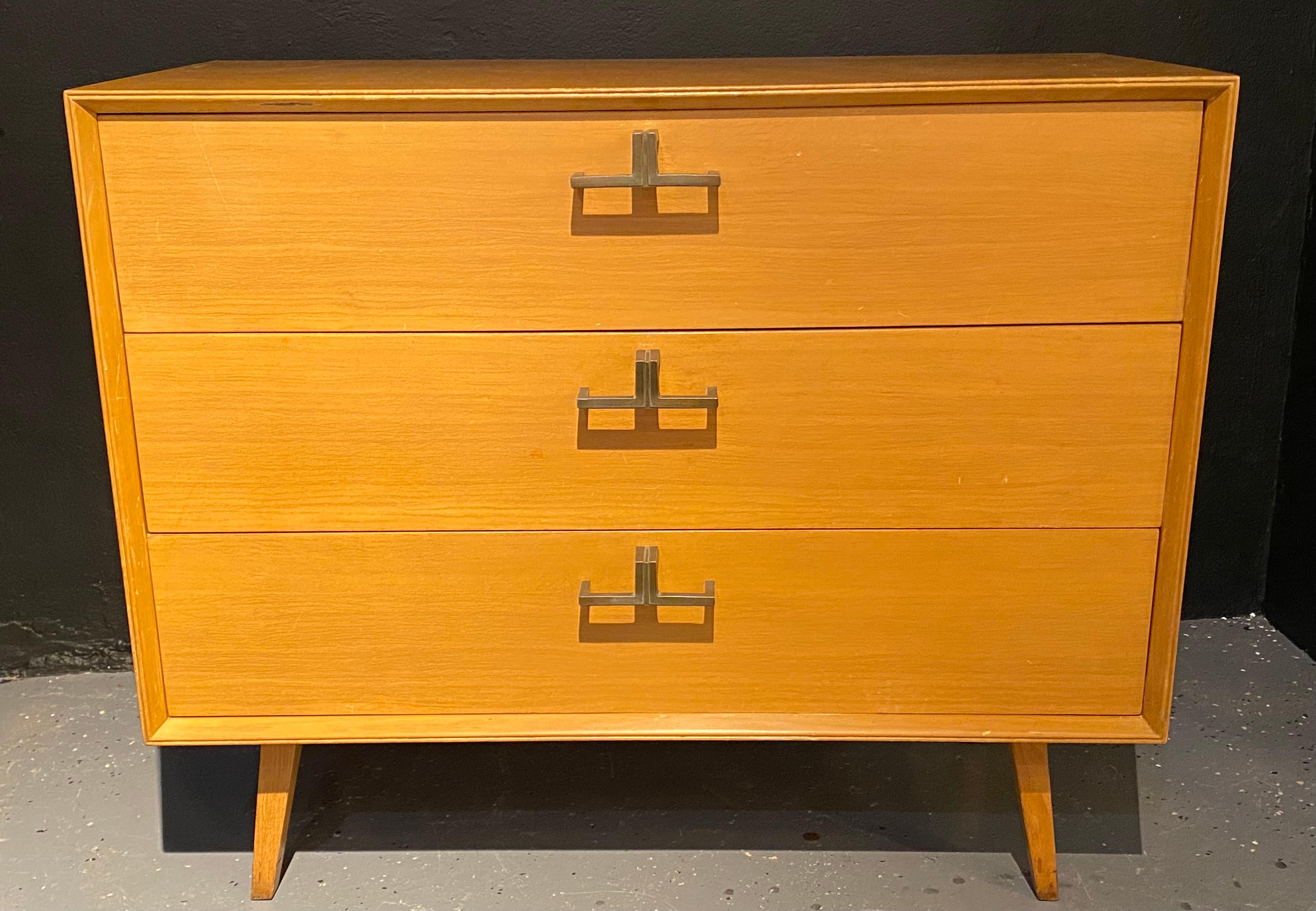 Pair of Mid-Century Modern bachelor chests, commodes, nightstands or dressers. A finely constructed pair of three-drawer commodes, all wood, with brass mounts having a sleek and simply flair. The pair with sprayed legs supporting a large case