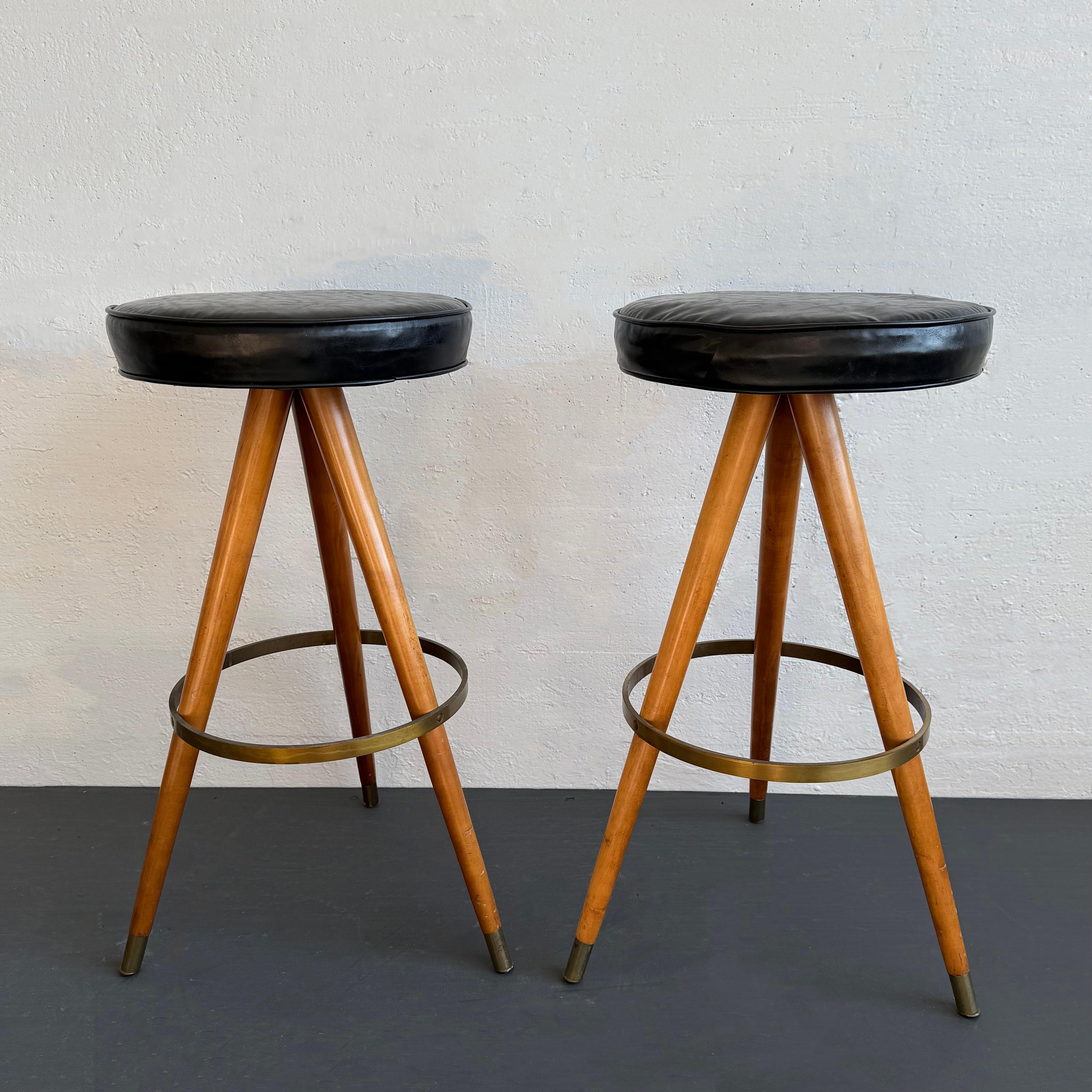 Cette paire élégante de tabourets de bar modernes du milieu du siècle frappe la quintessence de la silhouette rétro moderne. Ils sont dotés de sièges ronds en vinyle noir et de trois longs pieds en érable massif, évasés et effilés, avec des