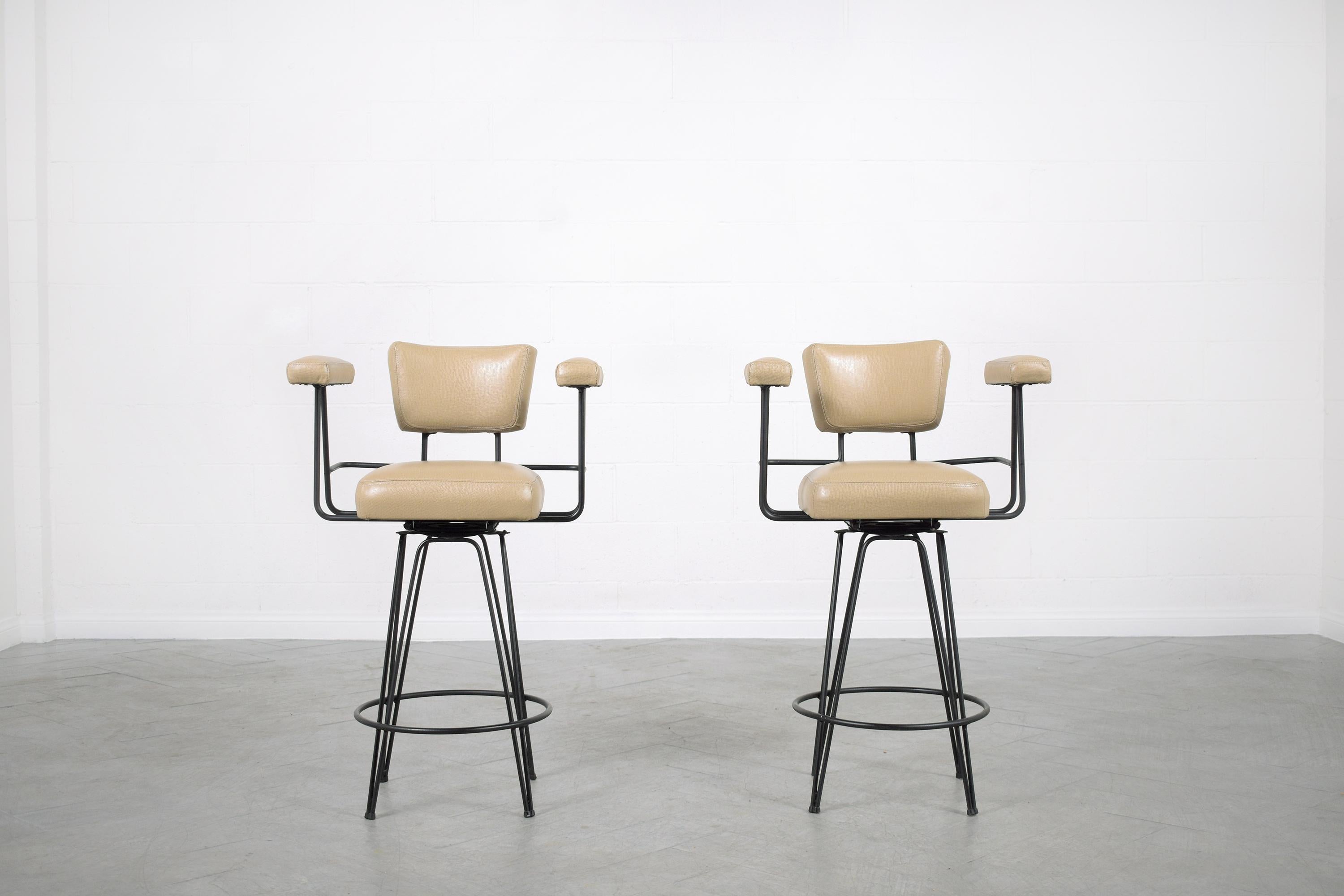 Elevate your home or living space with our stunning pair of Vintage Mid-Century Modern Swivel Barstools, a testament to classic design and expert craftsmanship. These barstools, handcrafted from robust wrought iron, have been meticulously restored
