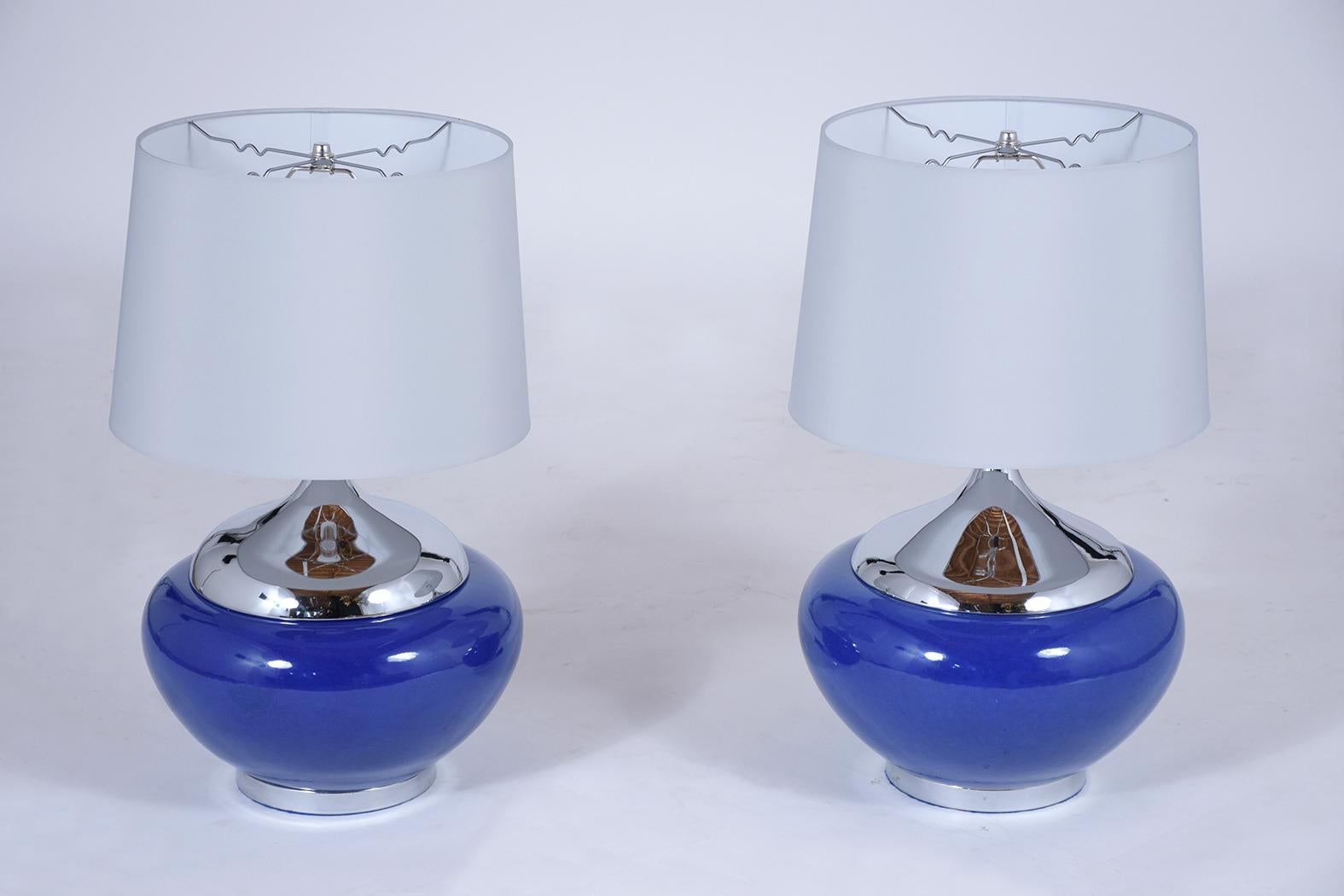 A fabulously handcrafted pair of midcentury table lamps that feature a ceramic enameled vase in blue color with a chrome neck and bottom. The pair comes with new, gray color fabric shades, and are wired to US standards in working condition. These