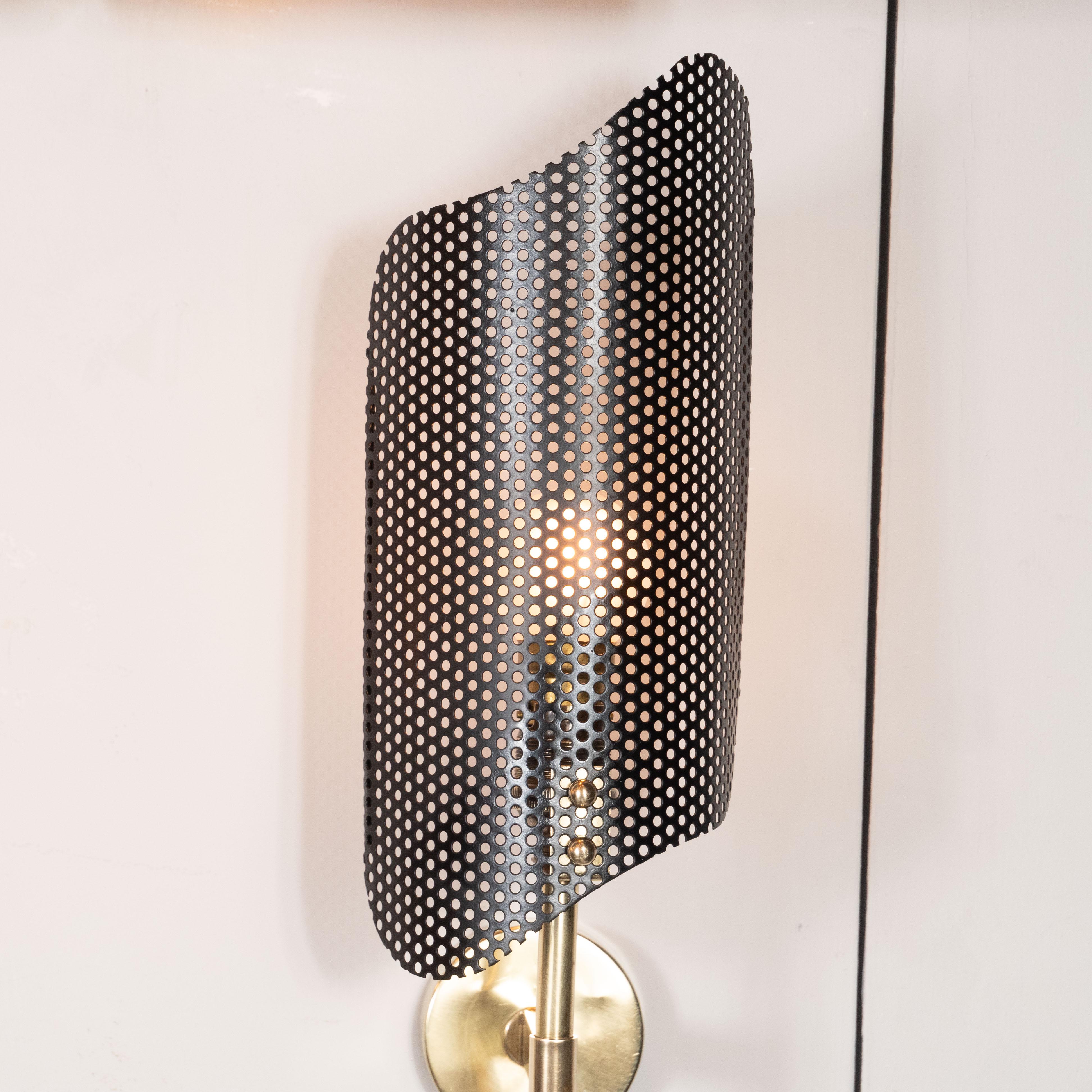 This refined sconce was realized in France, circa 1950 by the celebrated designer Mathieu Matégot.  It feature slender brass body that culminate in a pointed conical finial; rhomboid shades in perforated black metal; and a circular backplate also in
