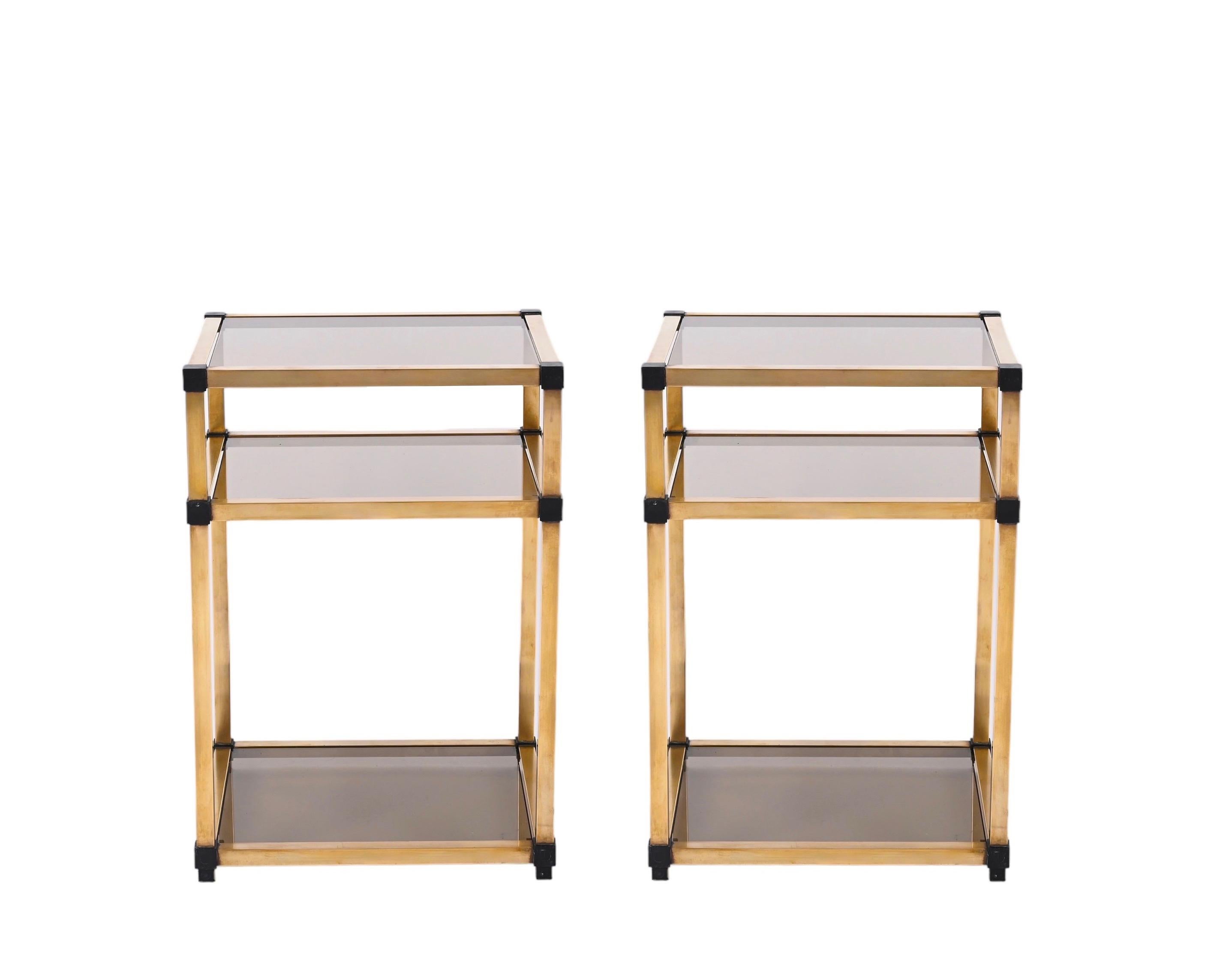 Gorgeous pair of Mid-Century Modern brass and smoked glass Nightstands, designed in Italy in the 70s.
These stunning bedsides feature a structure made in brass with black enameled corners and 3 shelves with smoked glasses. An incredibly elegant