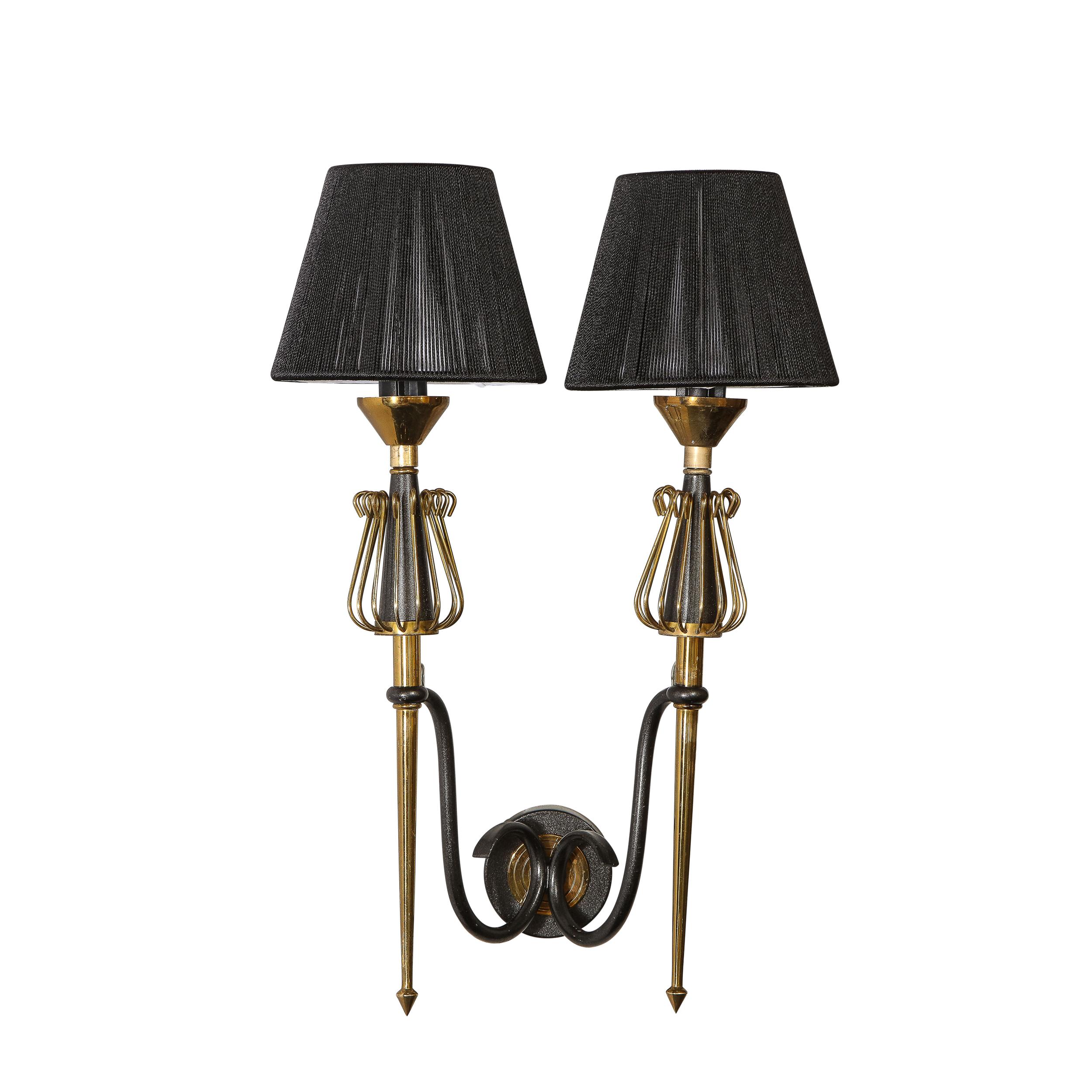This elegant pair of Mid-Century Modern sconces were realized in France circa 1950. They feature a circular back plate with curvilinear supports in black enamel emanating outwards that hold the tapered brass bodies of the sconces punctuated at their
