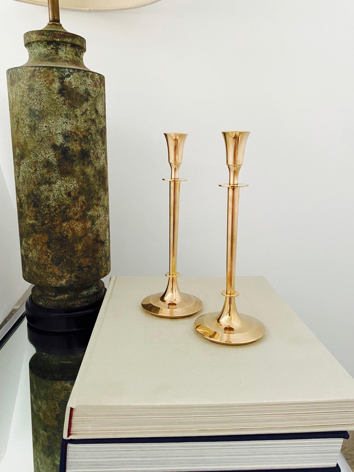 Pair of Swedish Mid-Century Modern candle holders cast in solid brass. The candlesticks have chic narrow stems with minimalist forms. The circular bases are tapered with beveled edges. Makes a beautiful addition to any tableware setting.