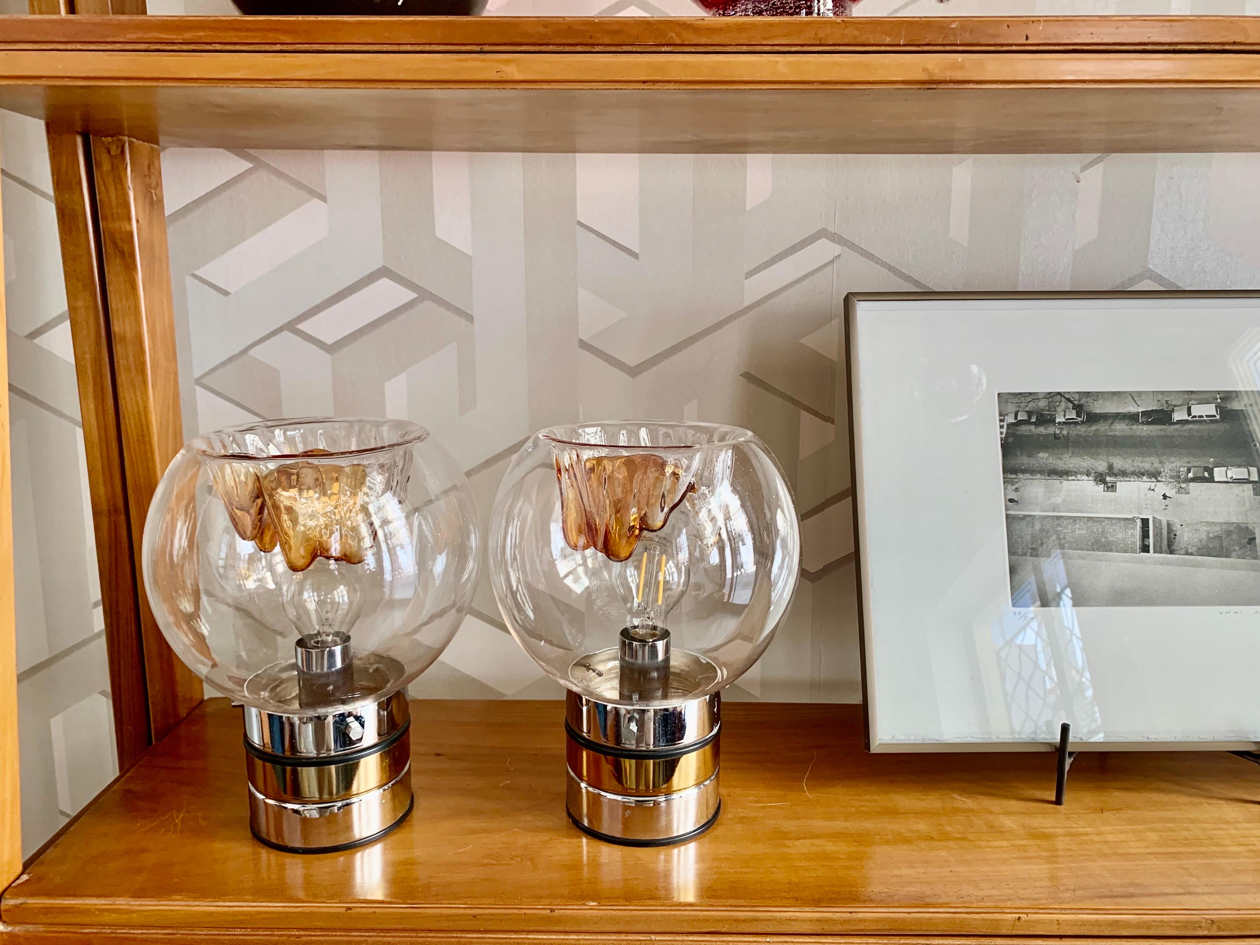 A pair of Mid Century Modern Table lamps by Mazzega, With the base in chromed metal and brass that supports the lampshade in Murano glass with brown shapes, they are vintage lamps in very good condition and easy to use in any space, they are rewired