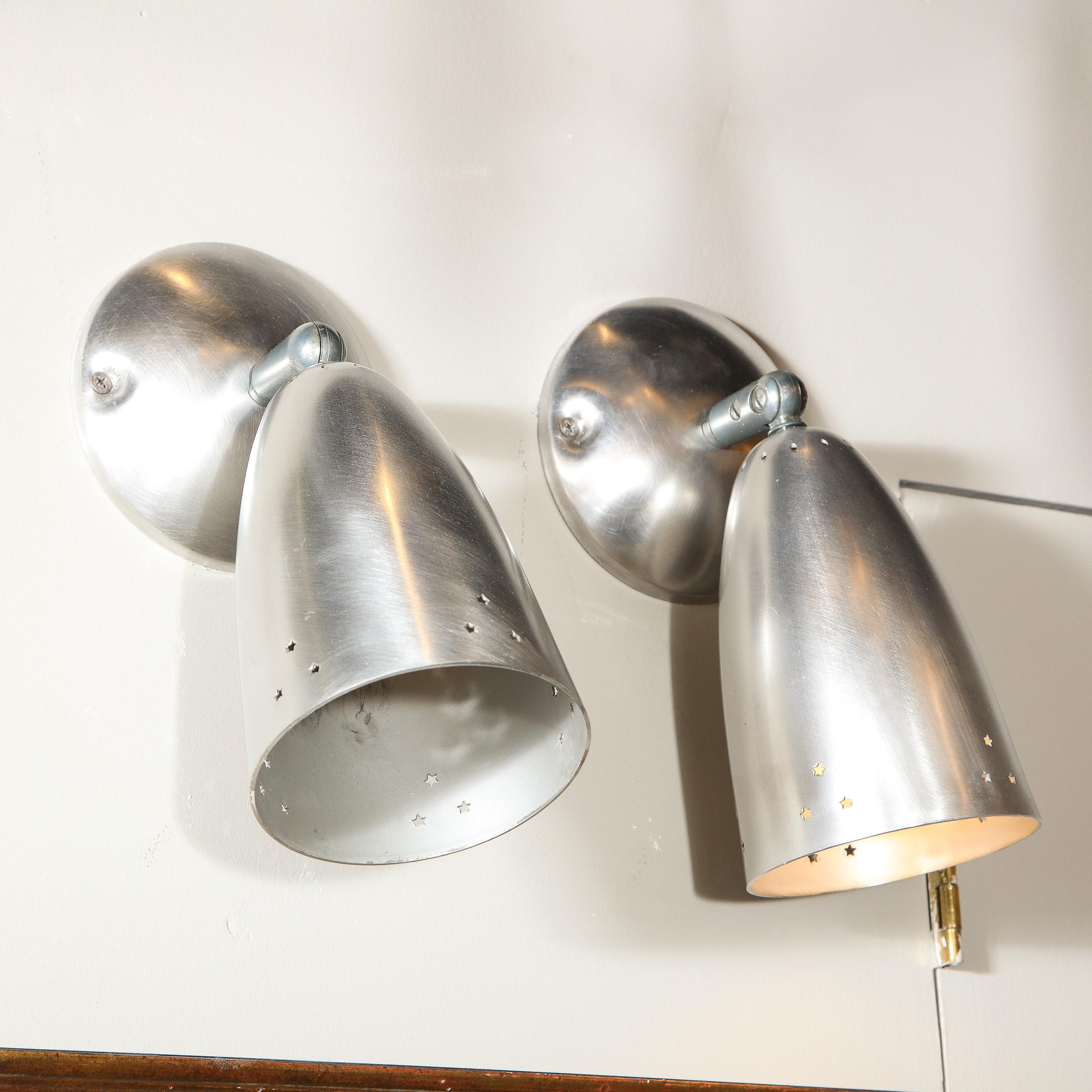 This refined pair of Mid-Century Modern articulating sconces were realized in the United States circa 1960. They feature conical shades that attach to subtly convex circular back plates via cylindrical supports. The shades offer pyramidal trios of