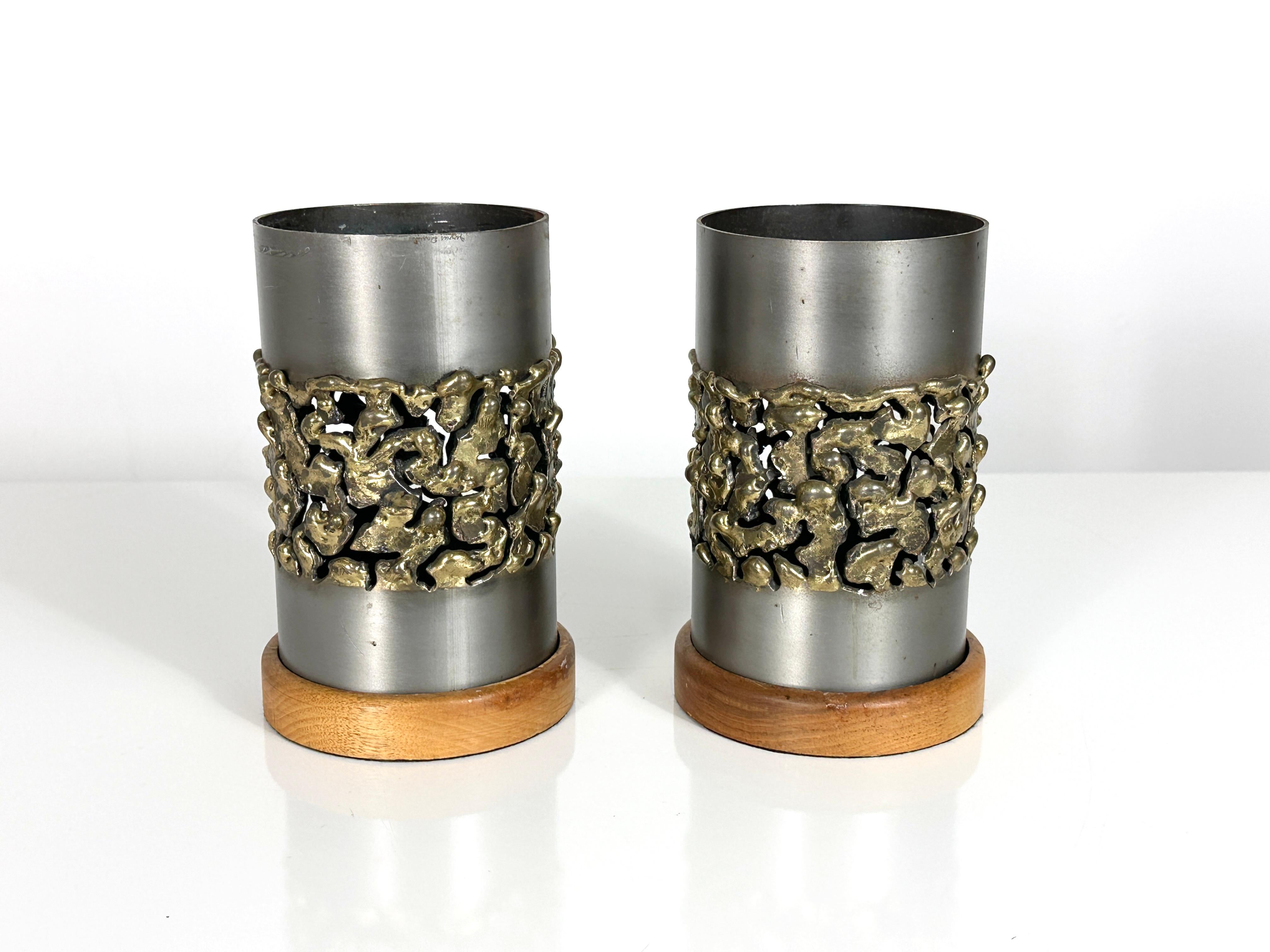A pair of sculptural mixed metal hurricane candle holders signed Jerry Davis circa 1970s

Cylindrical design in steel with torch cut brutalist applied brass detail
Inset into wood bases

Etched signature to upper rim

4