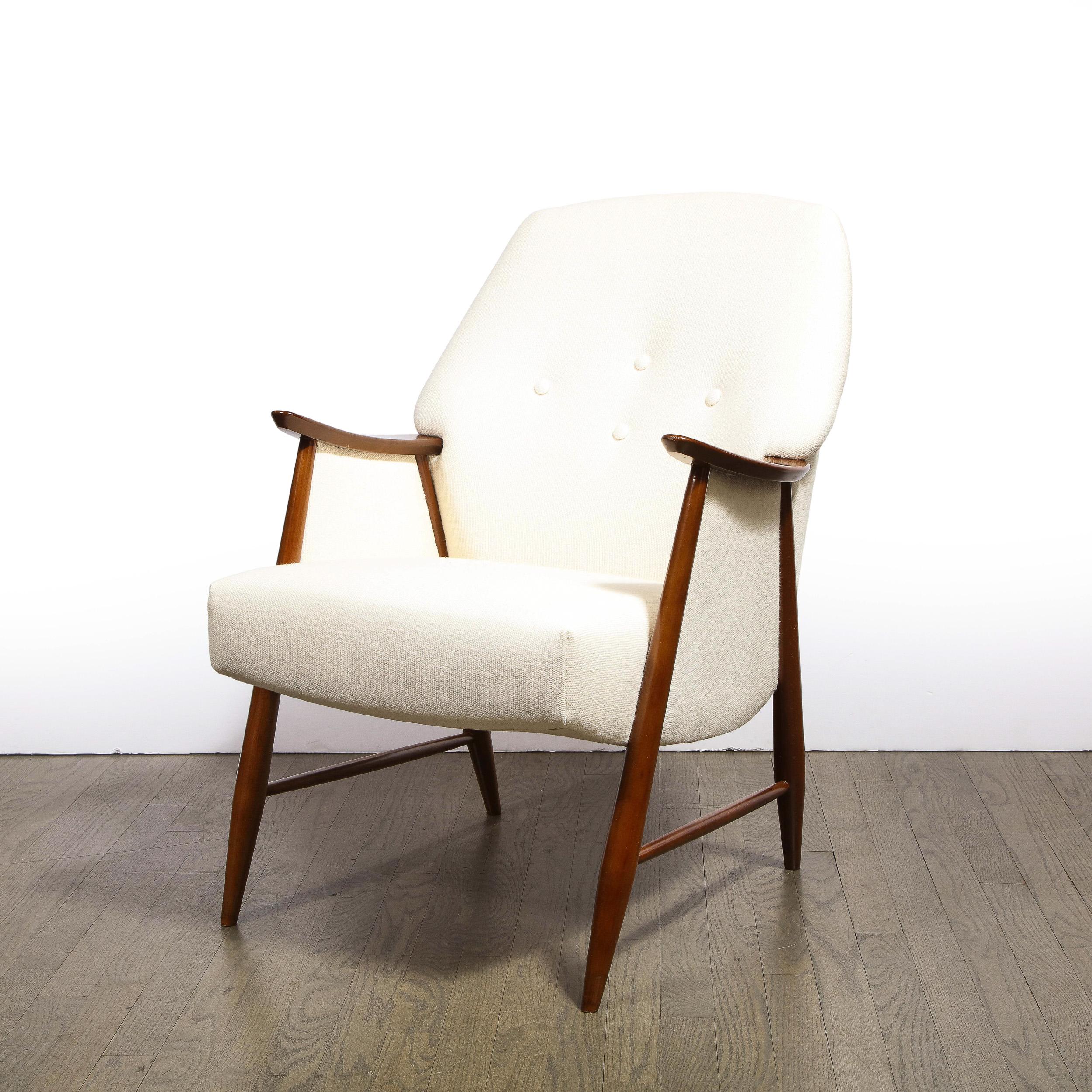This elegant pair of Mid-Century Modern arm chairs were realized in Sweden, circa 1950. They offer a graphic silhouette, boasting a hand rubbed walnut frame with splayed legs connected by a cylindrical cross slat; saddle arms (named for their