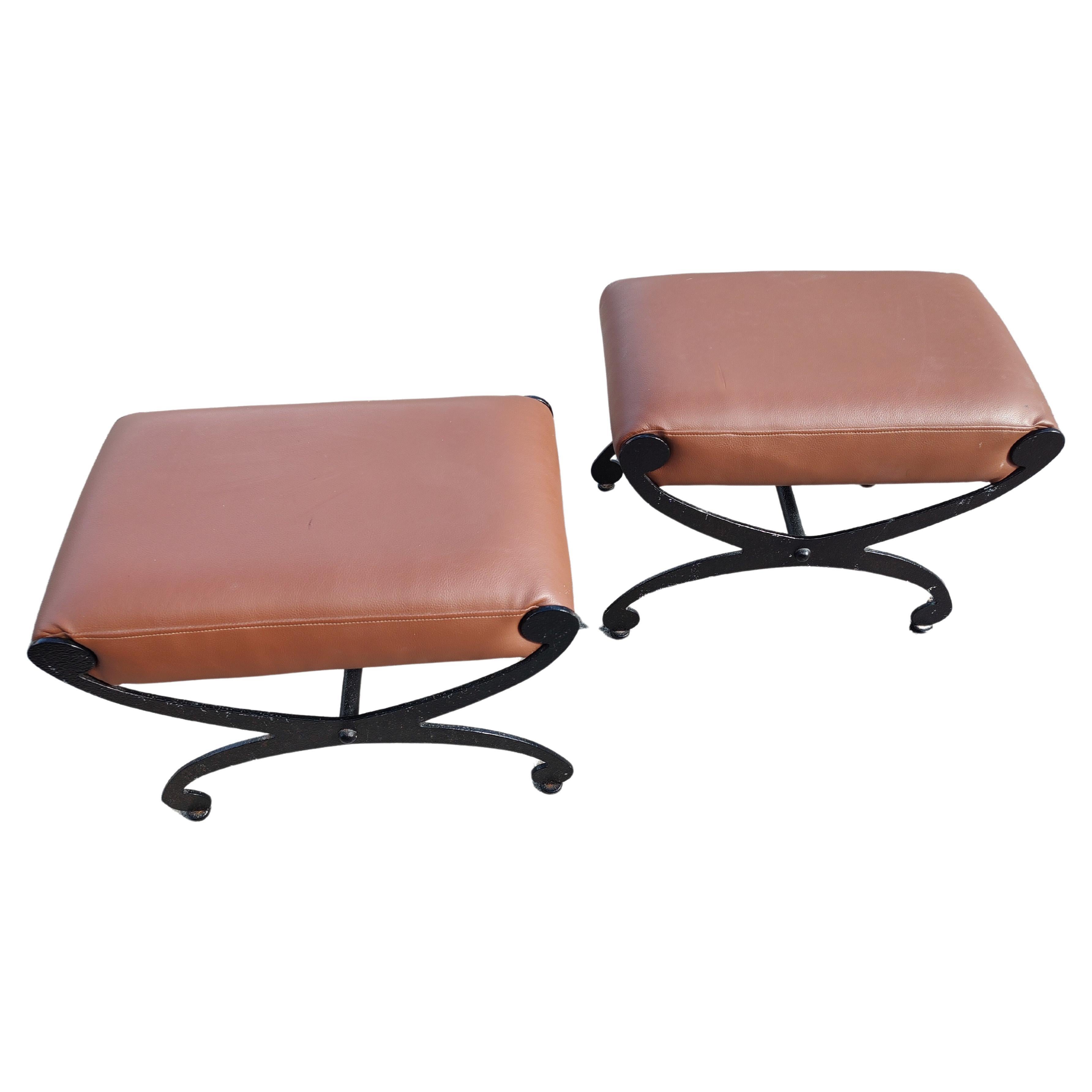 Fantastic pair of cast iron ottoman / footrests with tan brown Naughahyde. Curved X form with dimples in the iron that are currently painted black which can easily be repainted. In excellent vintage condition with a impression on the top of one the