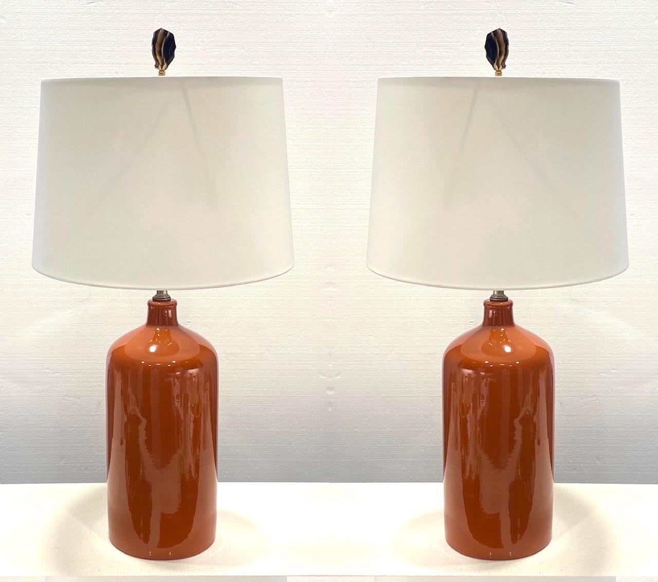 Pair of 1970s Mid-Century Modern handcrafted ceramic lamps with sleek ginger jar forms. Lamps have Minimalist cylinder pottery design with a glossy cognac or terracotta colored glaze finish. The lamp have brass fittings, and are shown with white