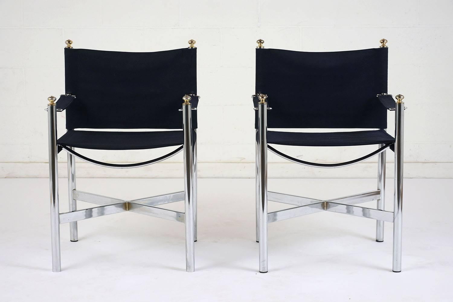 This pair of 1960s Mid-Century Modern lounge chairs feature a chrome-plated steel frame with brass finial accents. The frame has simple circular legs with an X-shaped stretcher bar and a curved seat bar. The seats are upholstered in a cobalt blue