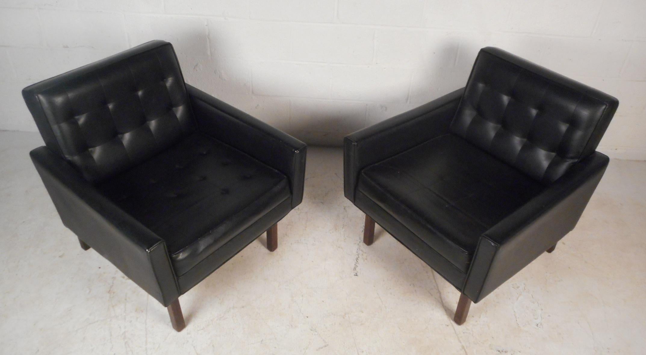 This stunning pair of vintage modern lounge chairs are covered in sleek black vinyl and sit on top of four sturdy walnut legs. A wonderful straight line design with low arm rests, wide back rests, and thick padded seating ensuring plenty of comfort.