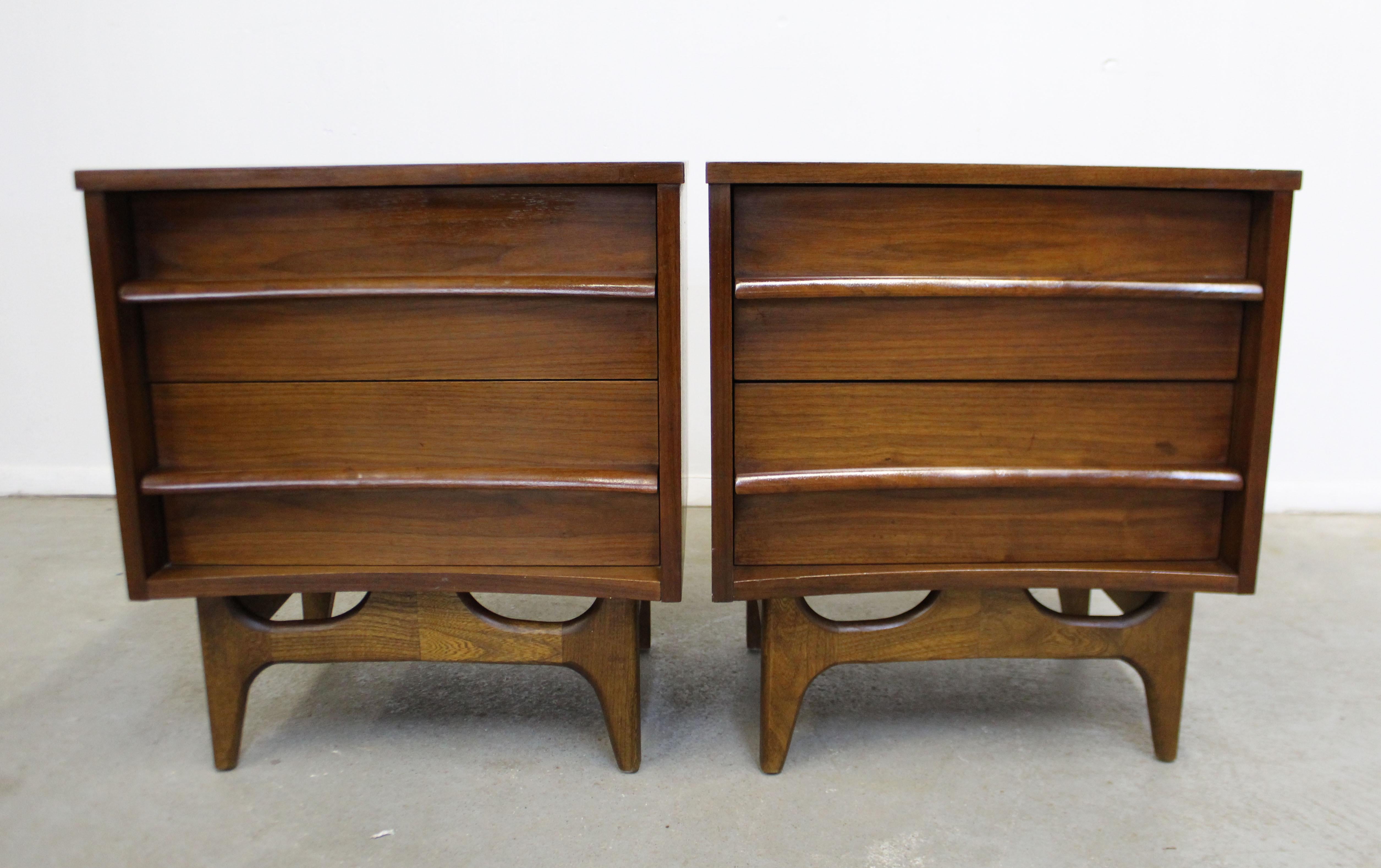 Offered is a beautiful pair of walnut nightstands with concave fronts and sculpted pulls. Includes two dovetailed drawers on each Stand. They are in very good vintage condition with slight surface scratches, small chips, and age wear. They are